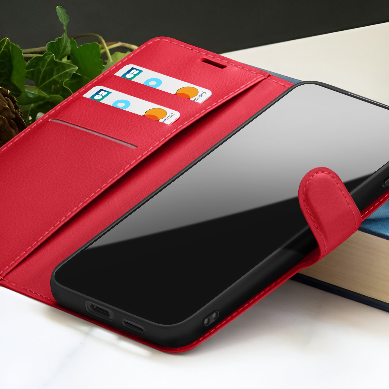 Een rode telefoonhoes met een zwarte telefoon erin. Creditcards zijn zichtbaar in de hoes. Een boek is zichtbaar op de achtergrond.