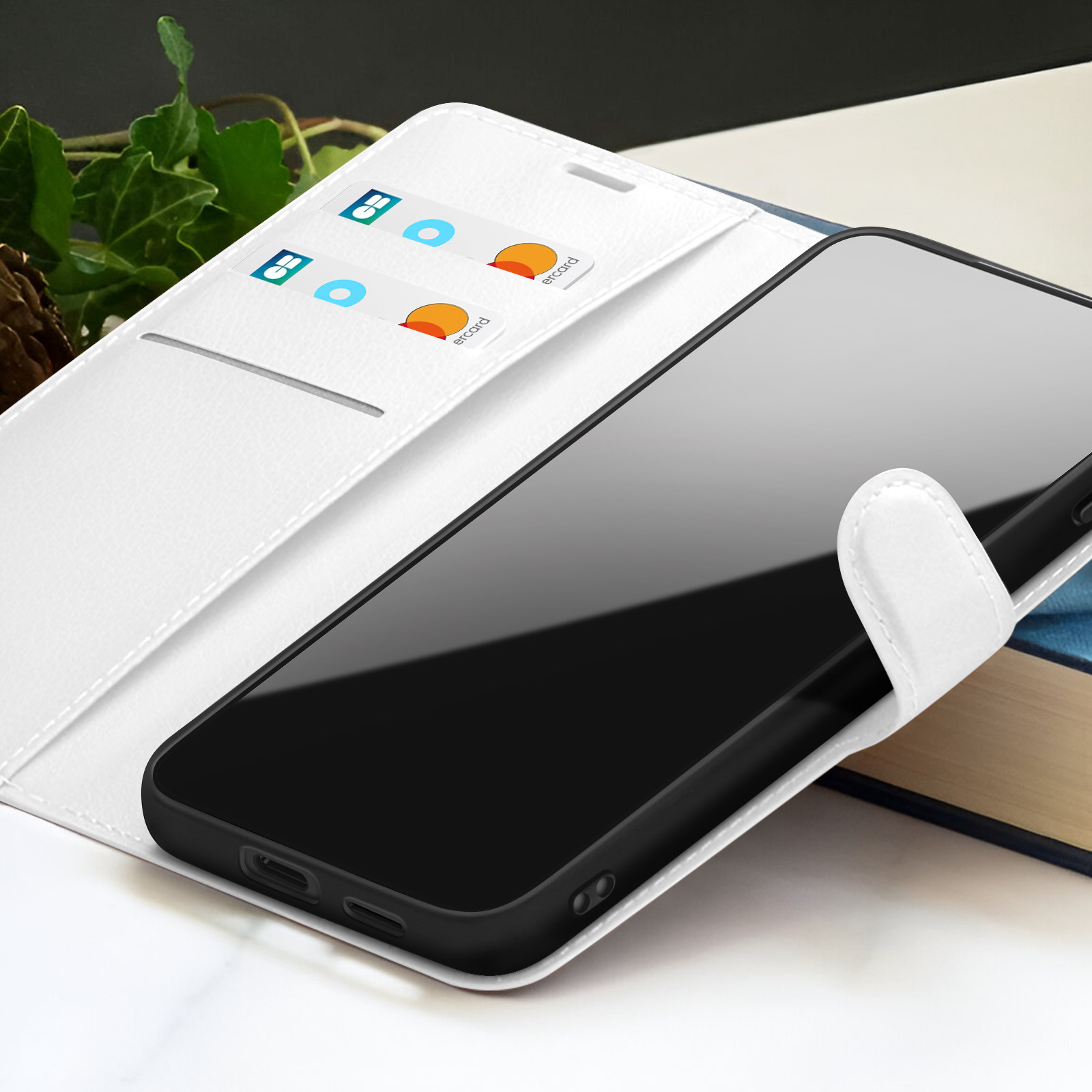 Étui de téléphone blanc avec fentes pour cartes de crédit, tenant un smartphone noir. Feuilles vertes et un livre en arrière-plan.