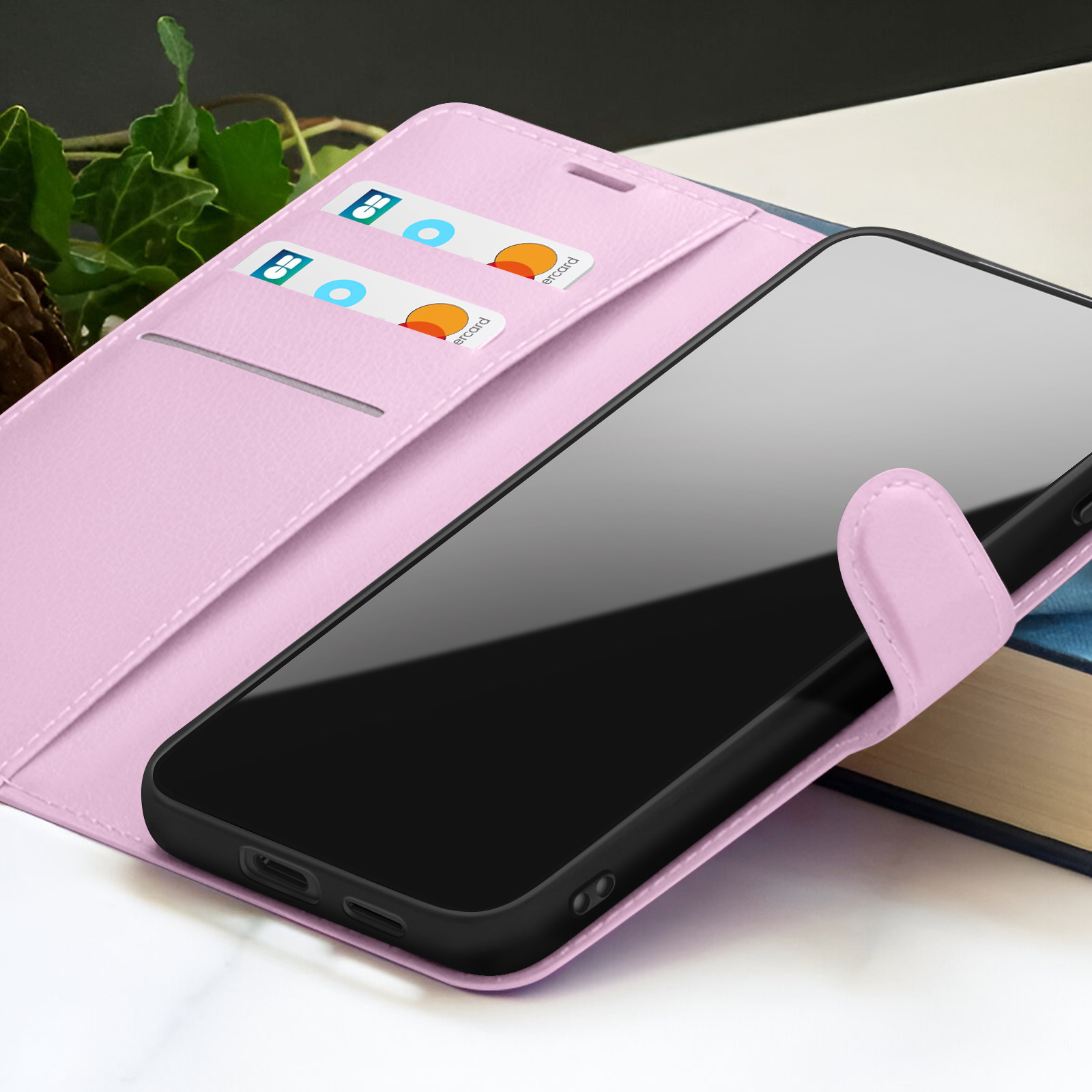 Étui de téléphone rose avec téléphone à l'intérieur. Cartes de crédit dans les fentes. Feuilles vertes en arrière-plan. Livre à droite.