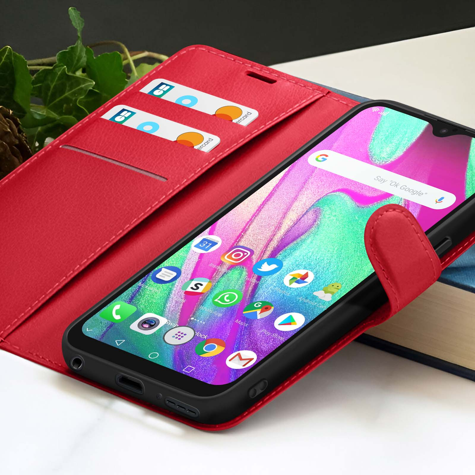 Smartphone in een rode hoes met kaarten en apps op het scherm. Telefoon ligt op een boek. Groene bladeren op de achtergrond.
