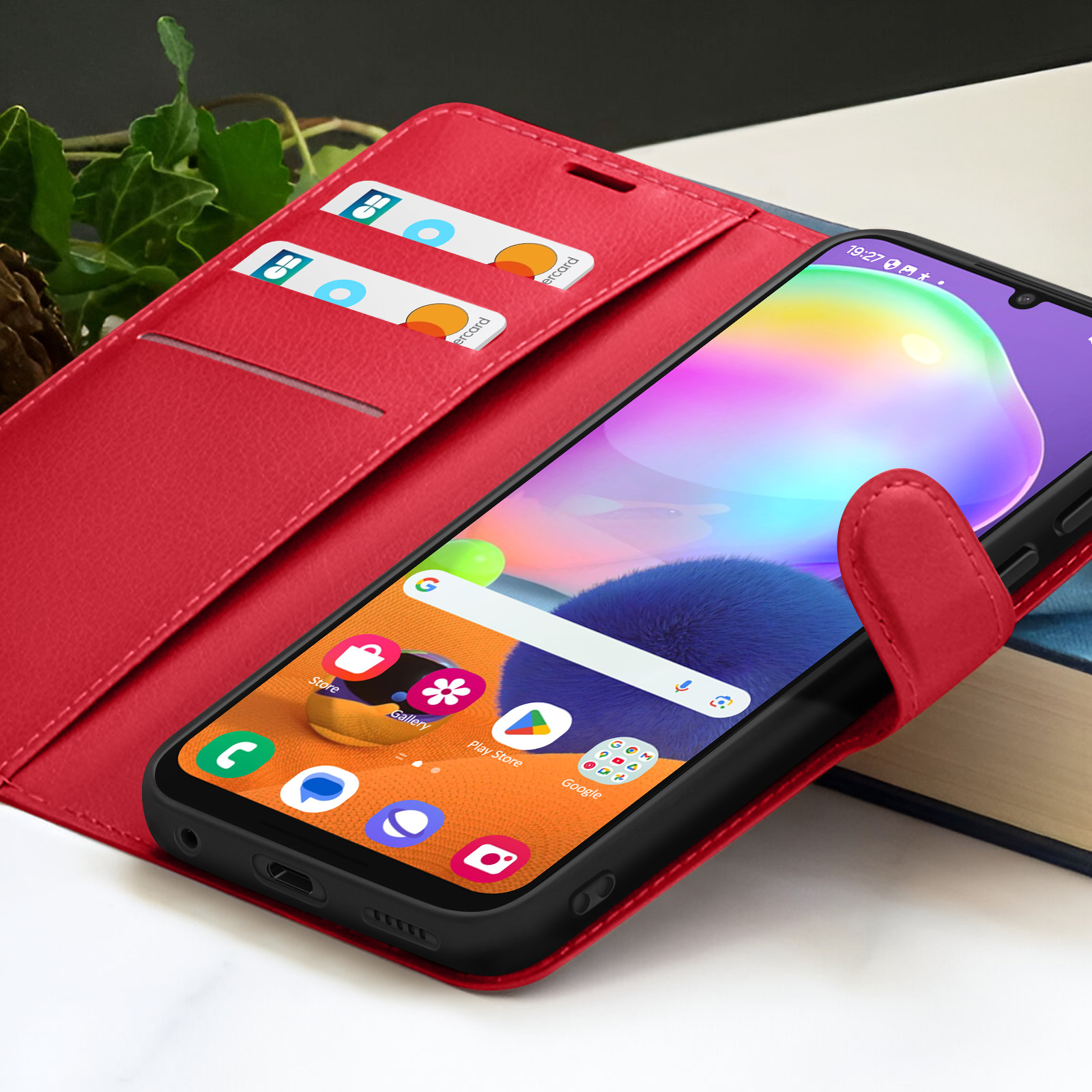 Un étui de téléphone rouge avec un téléphone affichant des applications. Cartes de crédit visibles. Arrière-plan flou, avec livres et feuilles.