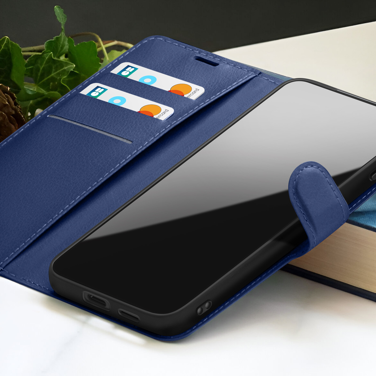 Un étui de téléphone bleu avec un téléphone à l'intérieur. Des cartes de crédit sont dans l'étui. Le fond a un livre et des feuilles vertes.