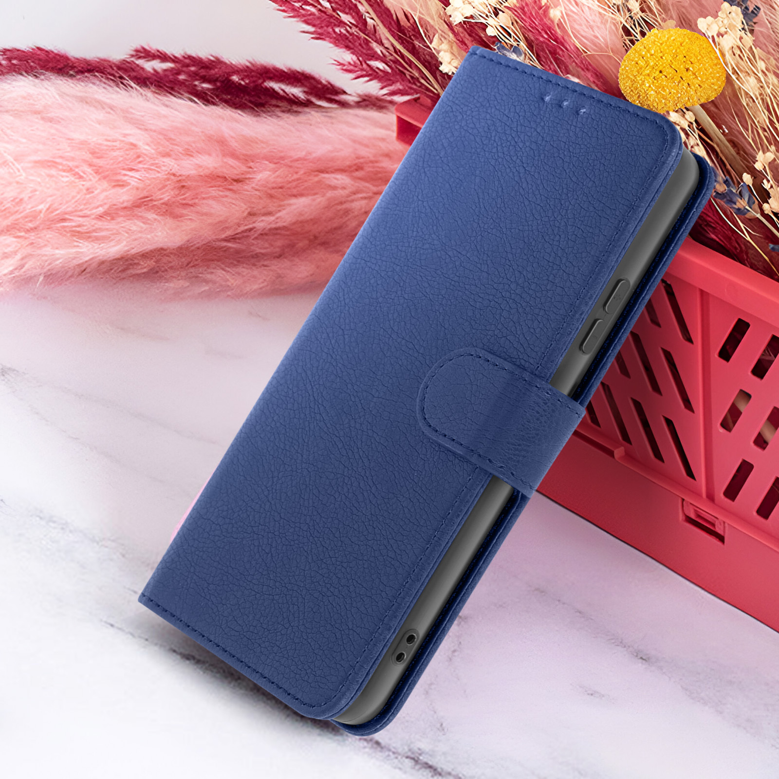 Étui de téléphone en cuir bleu sur surface en marbre. Accents floraux roses et rouges en arrière-plan.