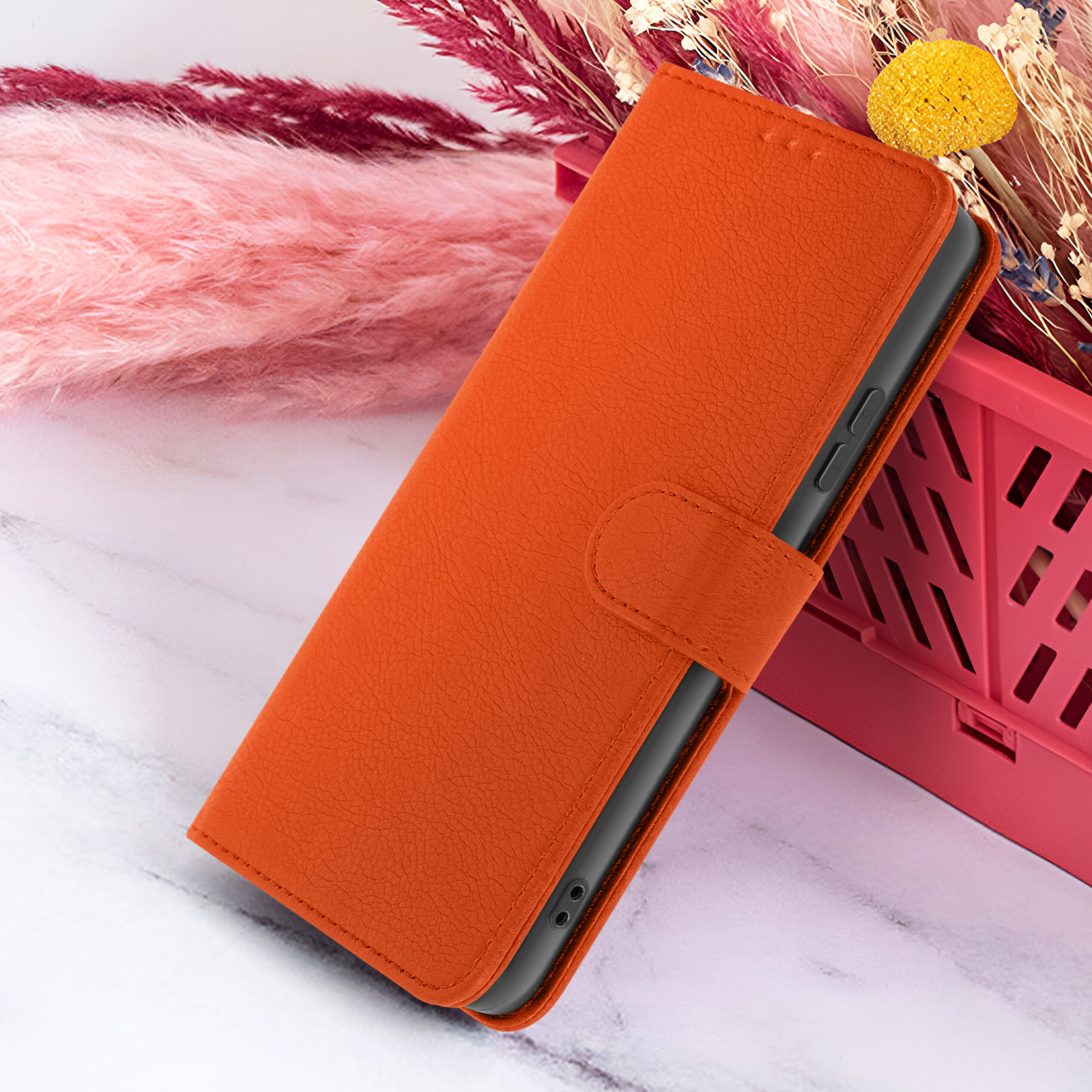 Un étui de téléphone orange est ouvert, révélant le téléphone à l'intérieur. Éléments floraux roses et jaunes en arrière-plan.