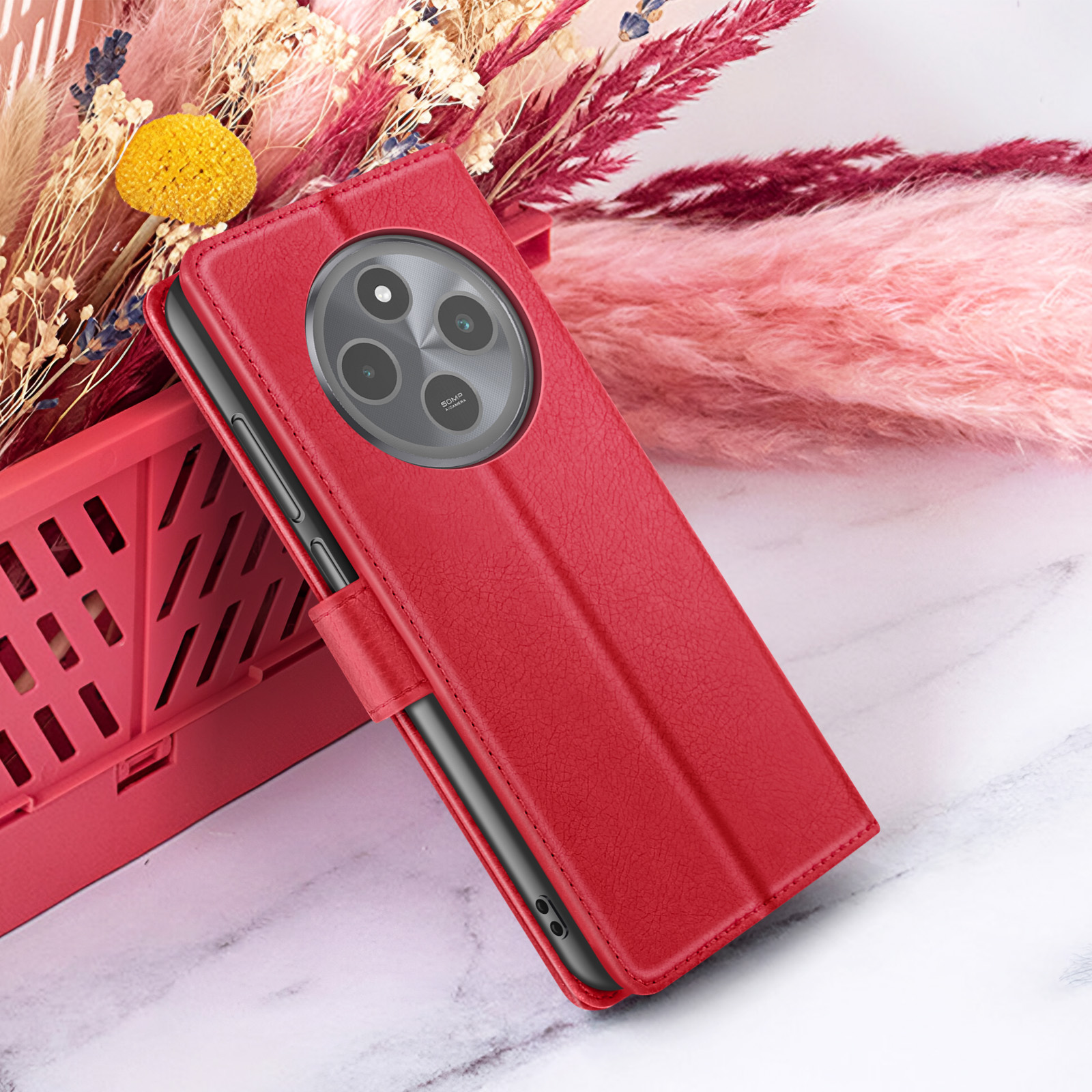 Étui de téléphone rouge avec découpe pour appareil photo, sur une surface en marbre avec arrangement floral rose et beige en arrière-plan.