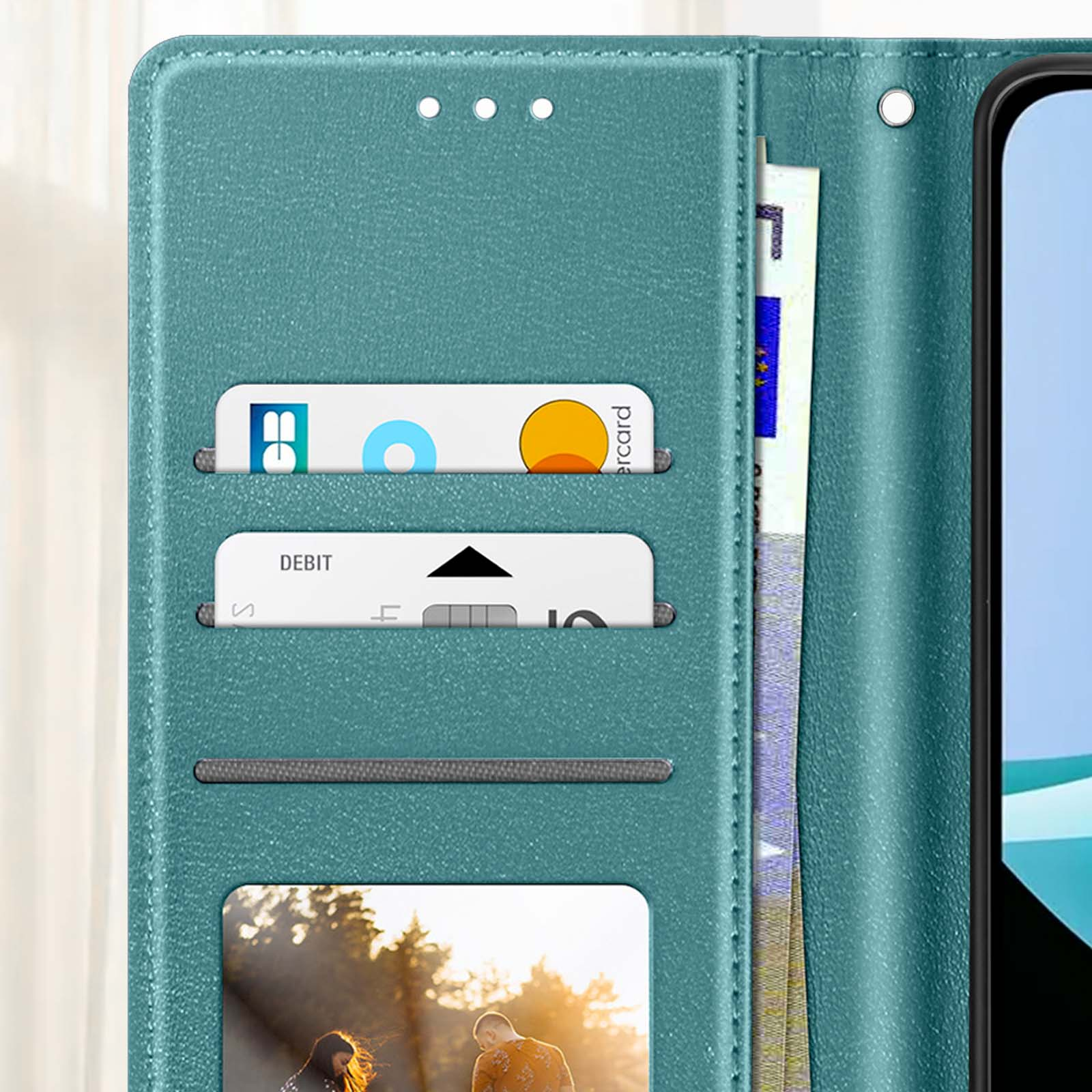 Una funda de teléfono verde azulado con ranuras para tarjetas, que contiene tarjetas y efectivo. Un teléfono es parcialmente visible a la derecha.