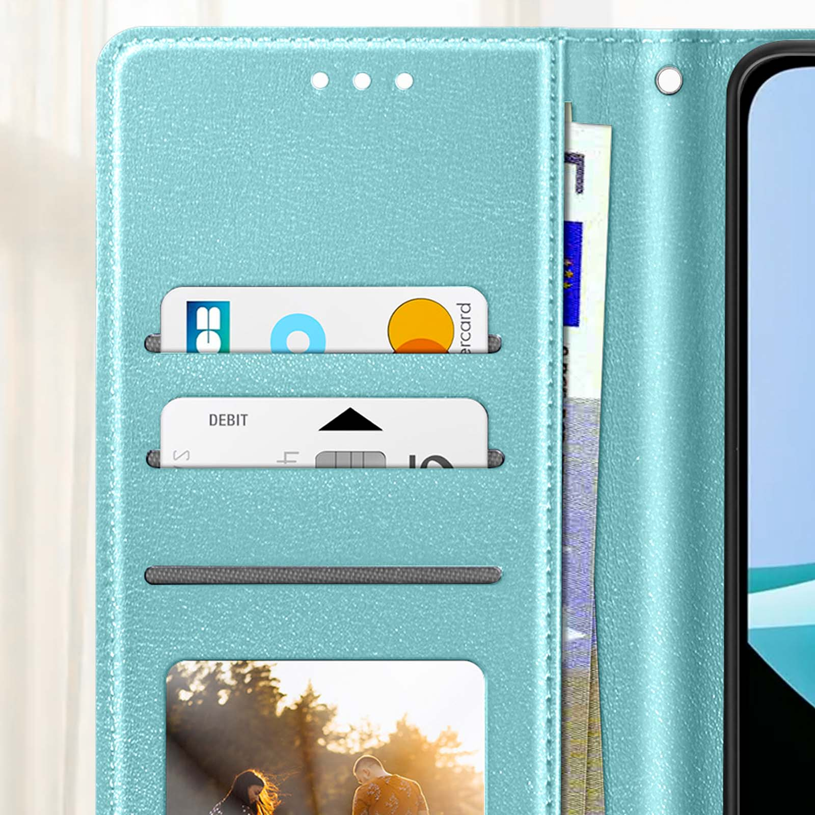 Un portafoglio per telefono color verde acqua con fessure per carte, contenente carte, denaro e una foto. Un telefono è a destra.