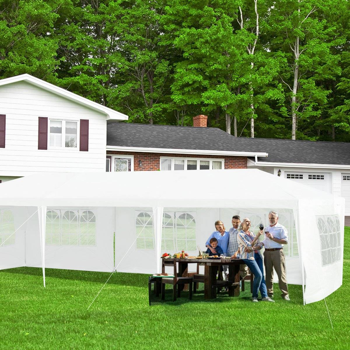 Reunión familiar bajo una carpa blanca en un jardín. Gente alrededor de una mesa con comida y bebidas, frente a una casa.