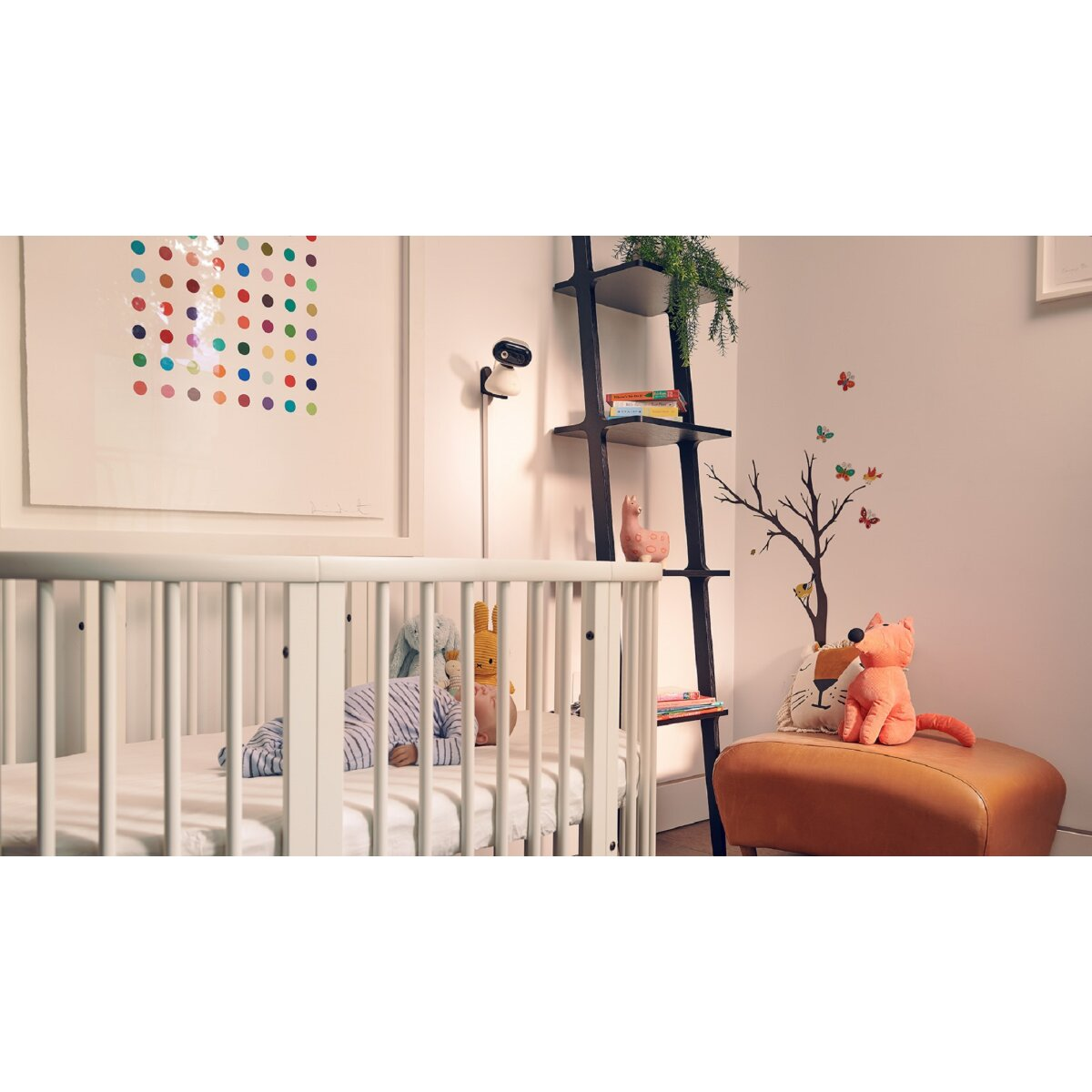 Un bambino in una culla con giocattoli, un dipinto sul muro, una scala a pioli e un pouf con un peluche a forma di volpe.