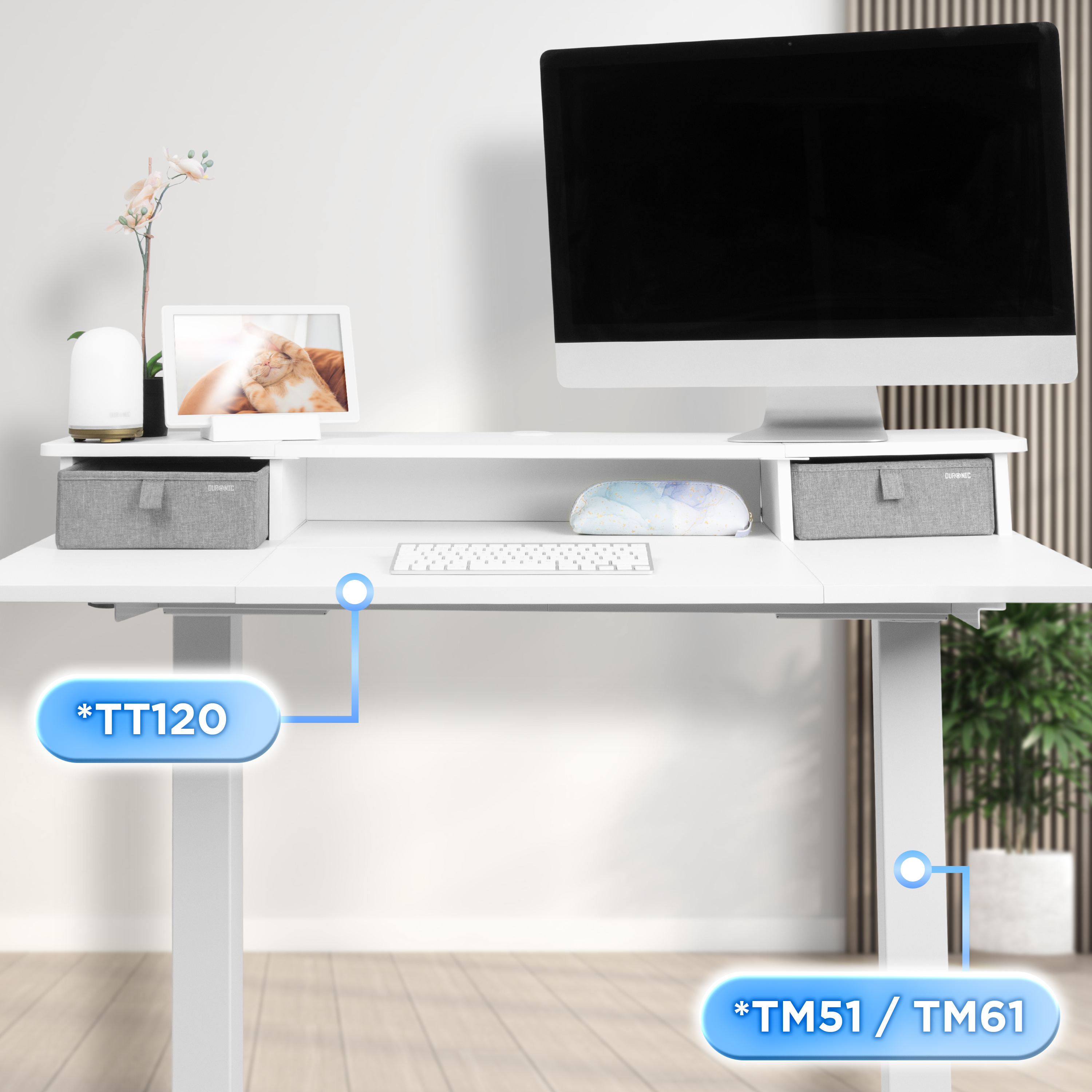Ein weißer Schreibtisch mit Monitor, Tastatur und Aufbewahrungsboxen. Eine Pflanze und ein Bilderrahmen sind ebenfalls vorhanden.