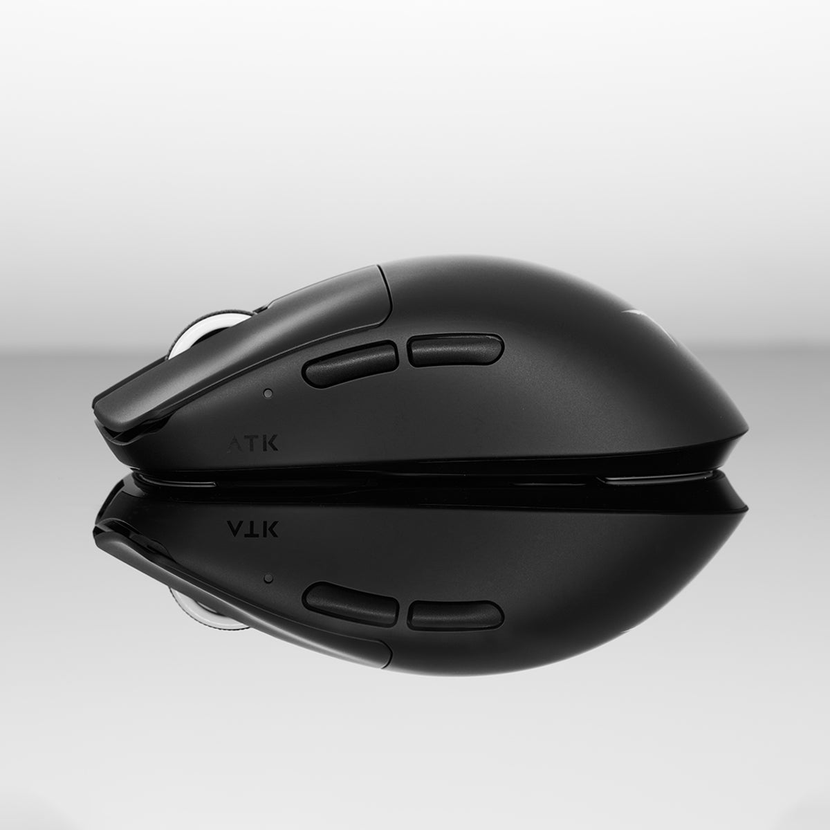 Un mouse per computer nero si riflette su una superficie lucida. Il mouse ha pulsanti e una rotella. 'ATK' è stampato sul lato.