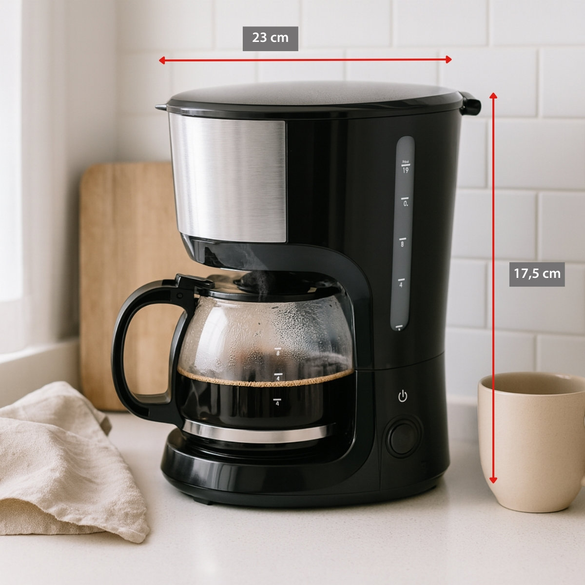 A black coffee maker with a glass carafe filled with coffee. A beige mug is beside it. A wooden board and a cloth are in the background.