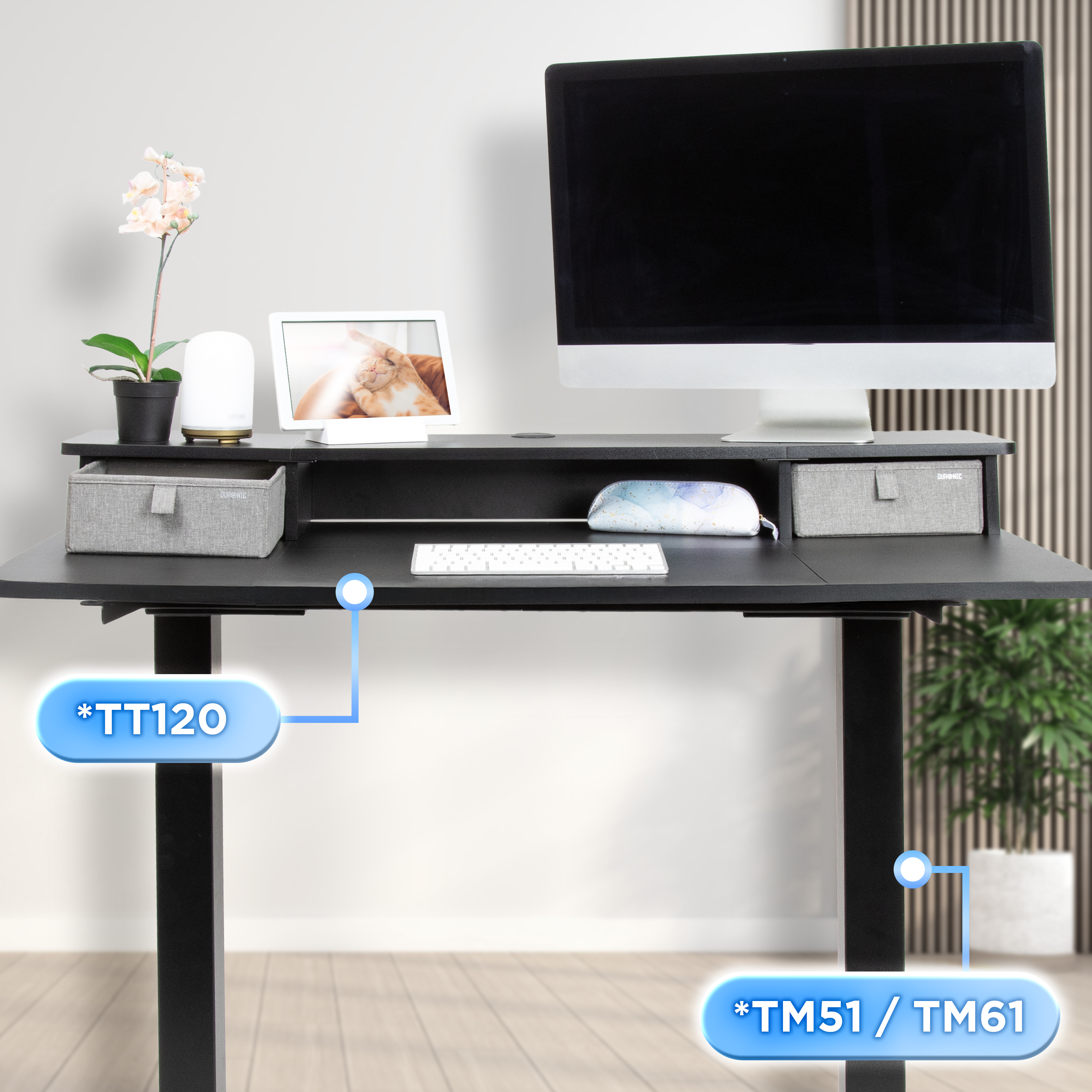 Ein schwarzer Schreibtisch mit Monitor, Tastatur und Zubehör. Eine Pflanze und ein gerahmtes Foto stehen auf dem Schreibtisch.