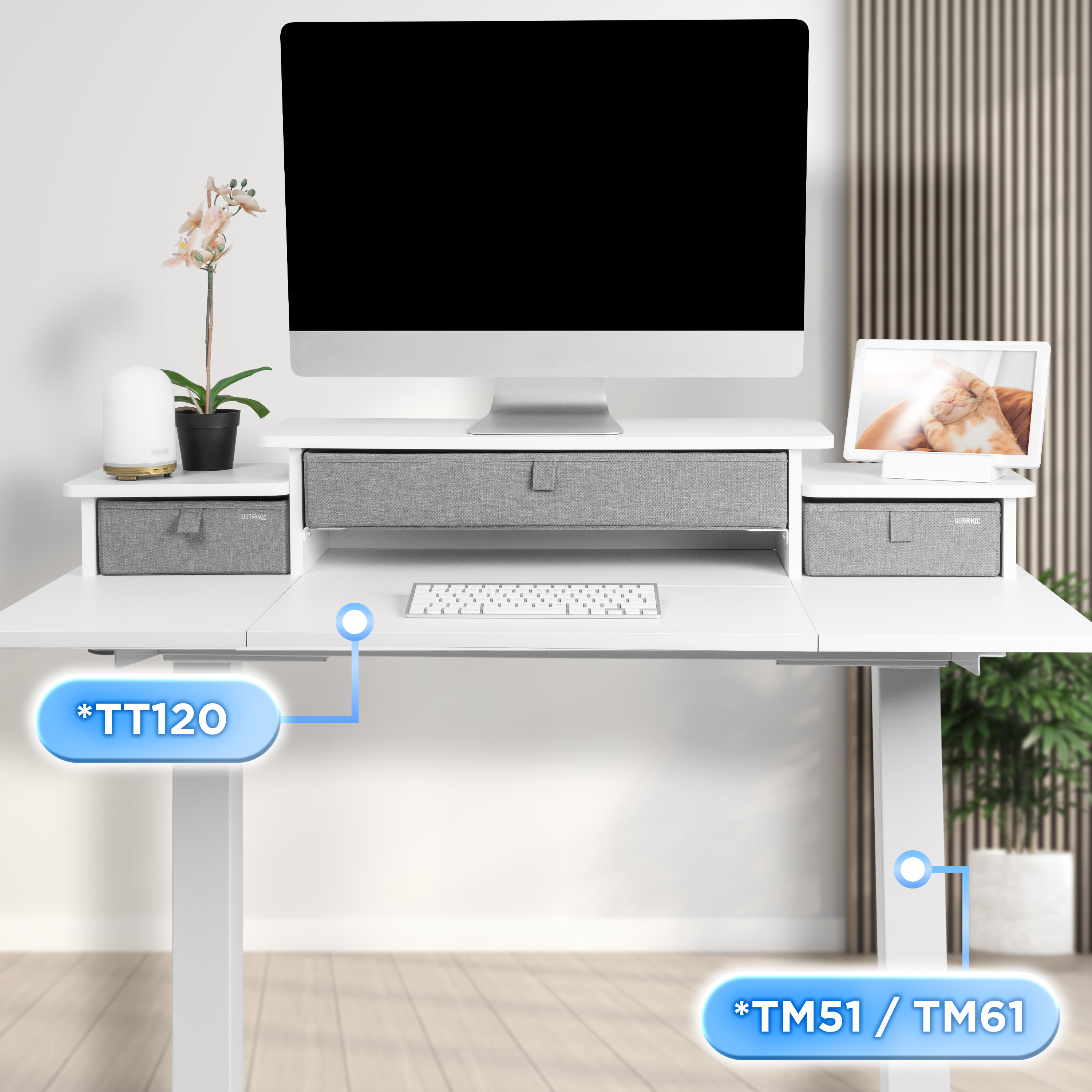 Ein weißer Schreibtisch mit Monitor, Tastatur und Schubladen. Rechts ist ein Katzenbild. Links sind Blumen und ein Luftbefeuchter.