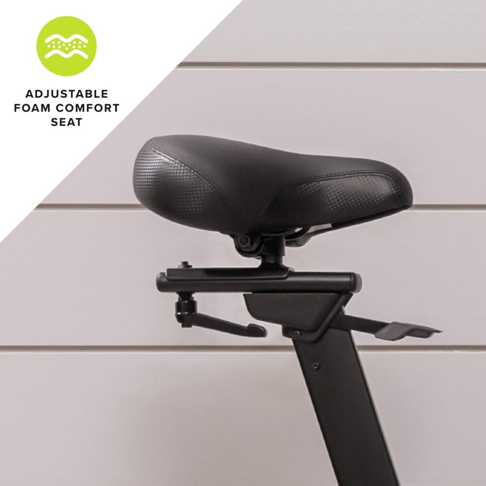 Black adjustable foam comfort seat of an exercise bike. White wall in the background.