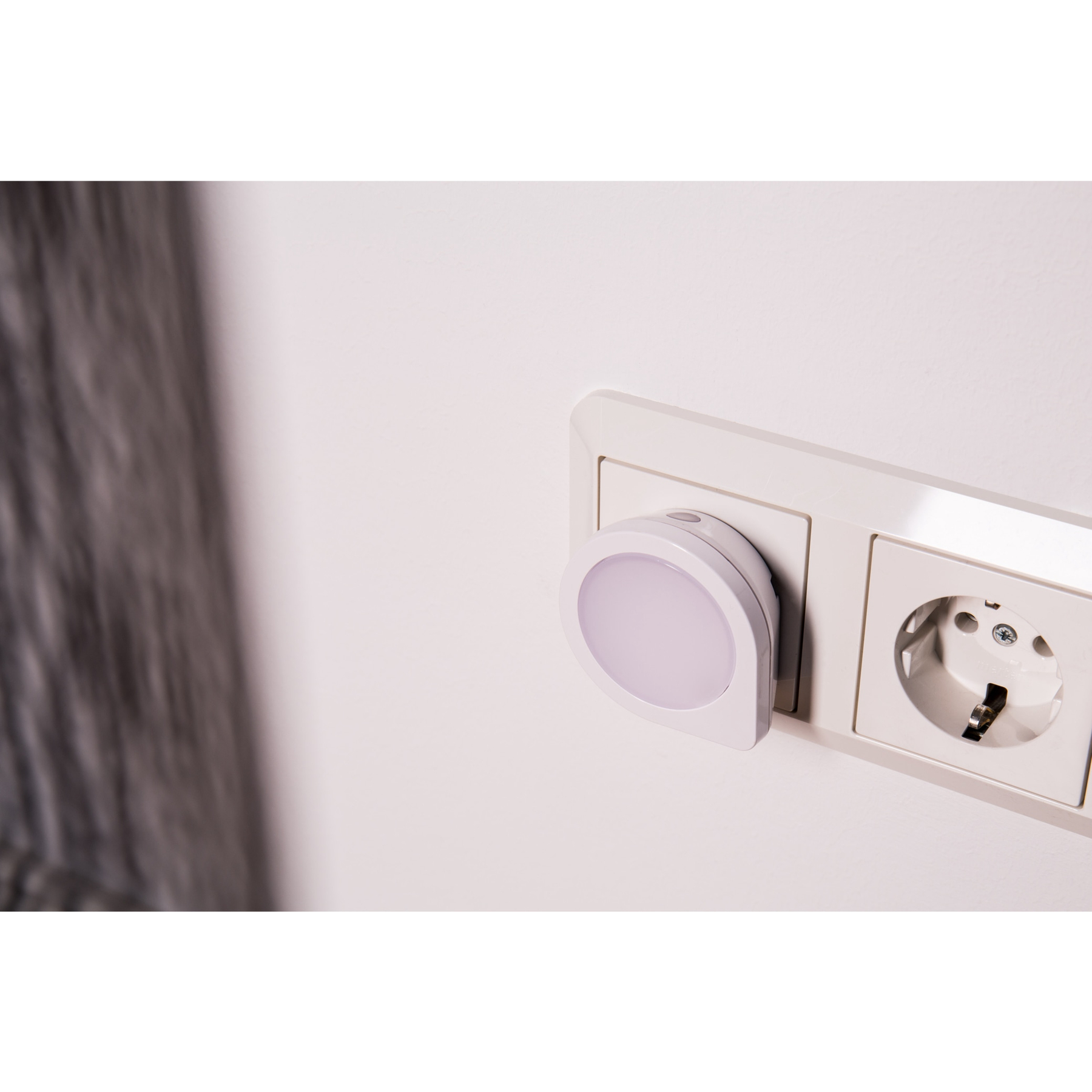 Un muro bianco con presa elettrica bianca e luce notturna collegata.