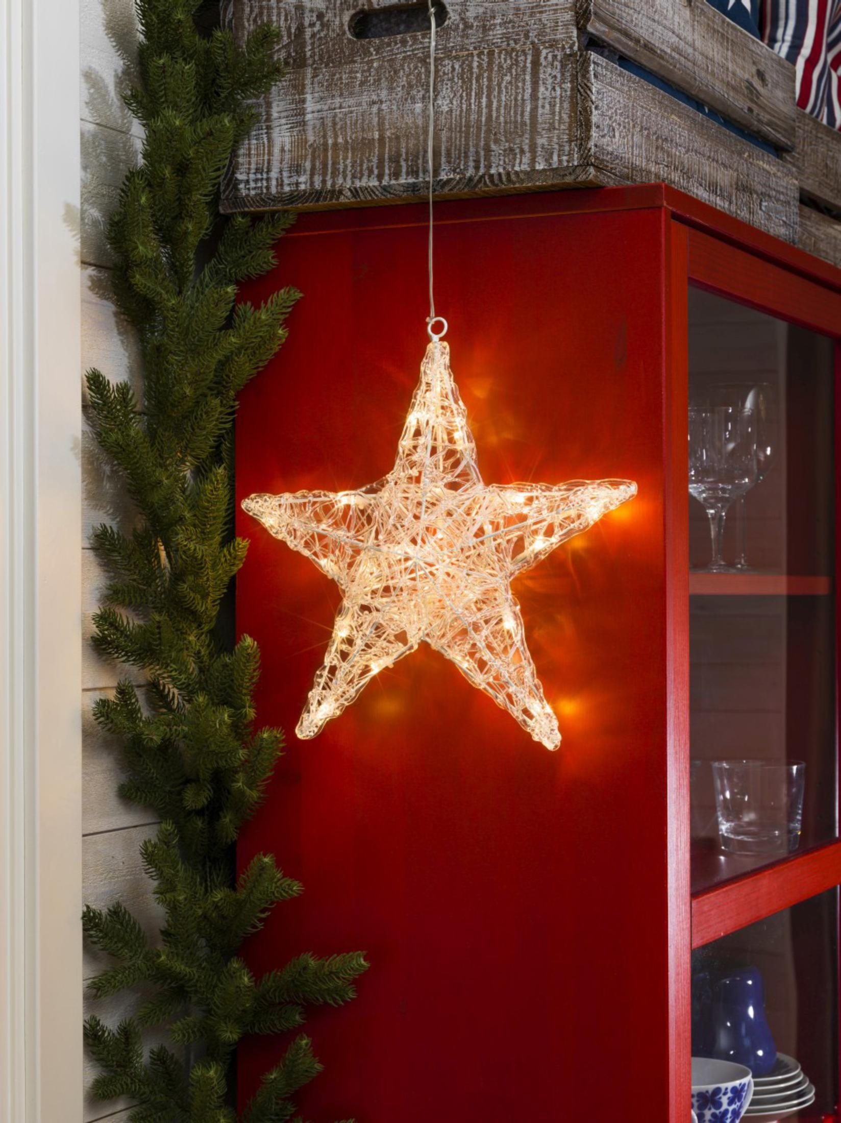 Una decorazione a stella illuminata è appesa contro un mobile rosso. Ghirlanda sempreverde a sinistra. Una cassa di legno è sopra il mobile.