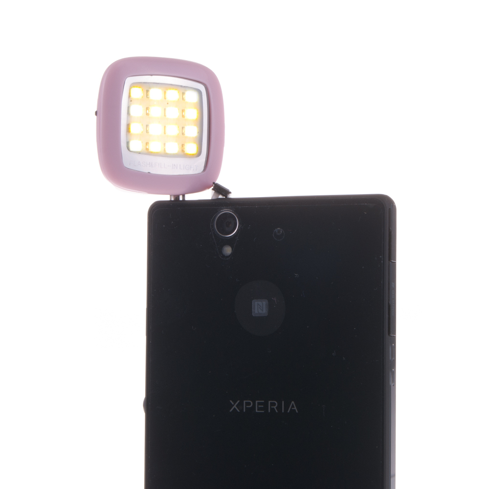 Un telefono Xperia nero con una luce di riempimento rosa chiaro collegata. La luce è quadrata con molte piccole luci a LED. Sfondo bianco.