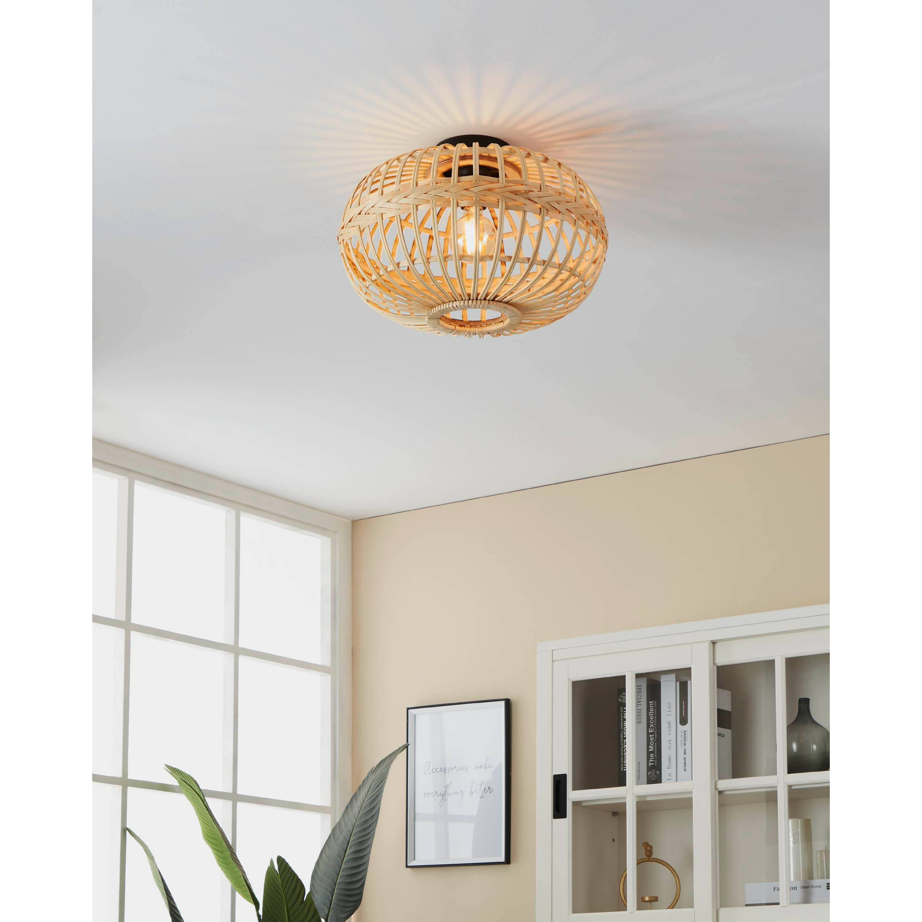 Una lampada da soffitto in rattan intrecciato illumina una stanza. Sullo sfondo una finestra, un armadio e una pianta.