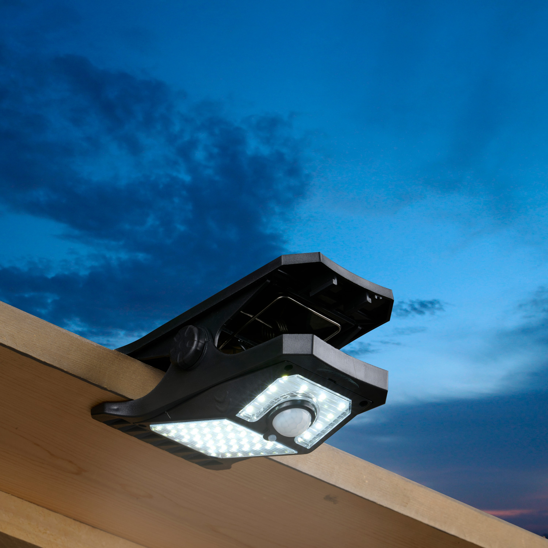 Zwarte zonnelamp met LED-verlichting bevestigd aan hout, tegen een blauwe en bewolkte lucht.