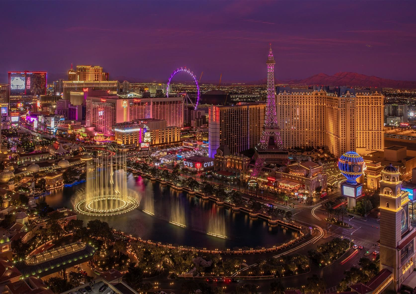 Otel ışıkları, dönme dolap ve Eyfel Kulesi replikasıyla Las Vegas'ın gece görünümü. Ön planda su fıskiyeleri.