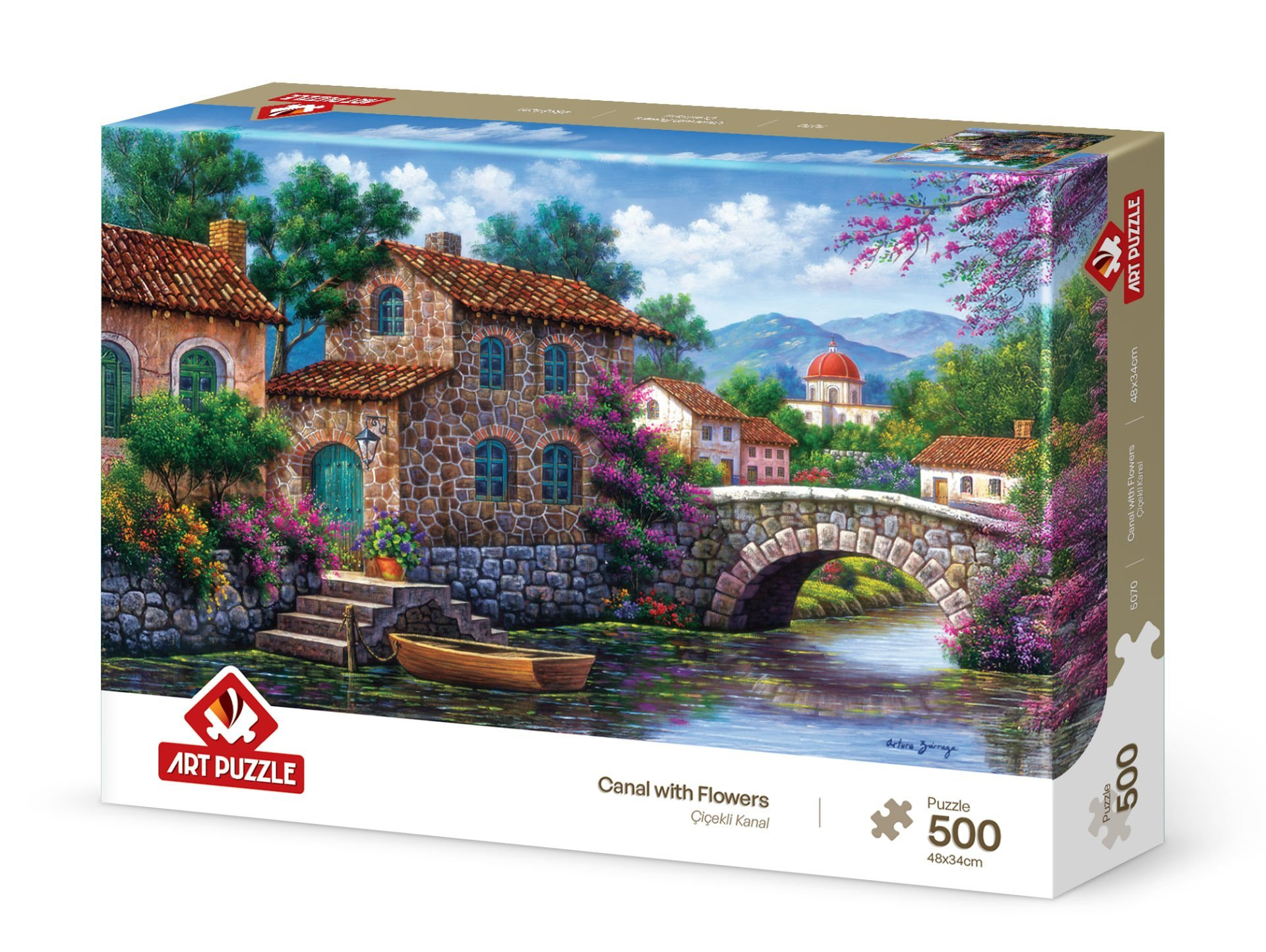 Una scatola di puzzle mostra una scena di canale con case in pietra, un ponte e fiori. Una barca è in acqua, sotto un cielo blu.