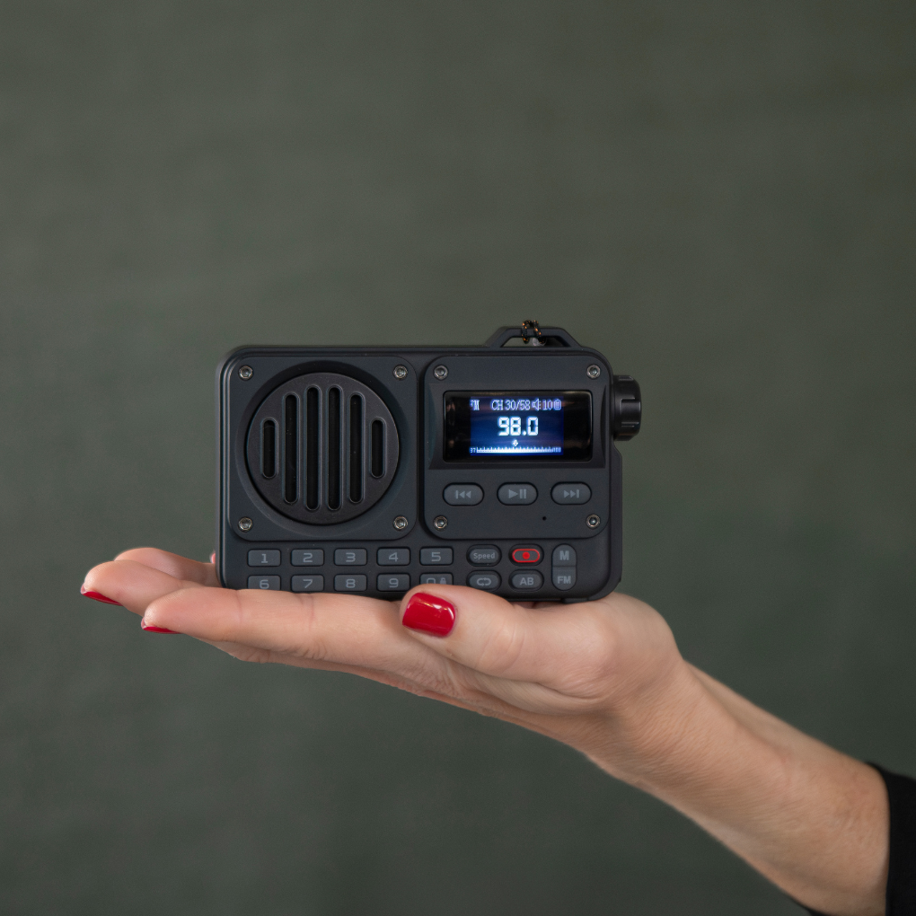 Una mano sostiene una pequeña radio negra que muestra '98.0'. La mujer tiene esmalte de uñas rojo. El fondo es verde apagado.