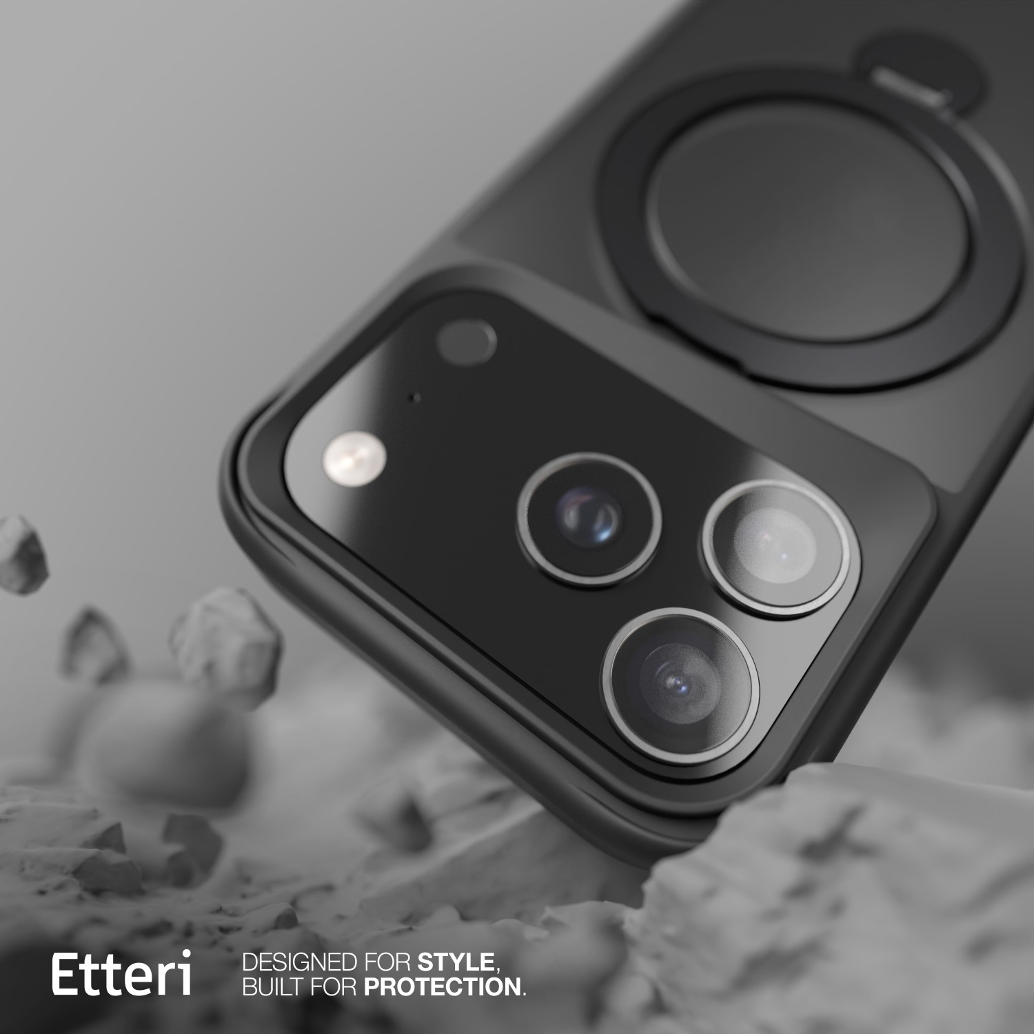 Primo piano di una custodia nera per smartphone. La custodia presenta un anello di supporto e più obiettivi della fotocamera. Lo sfondo è una superficie grigia strutturata.