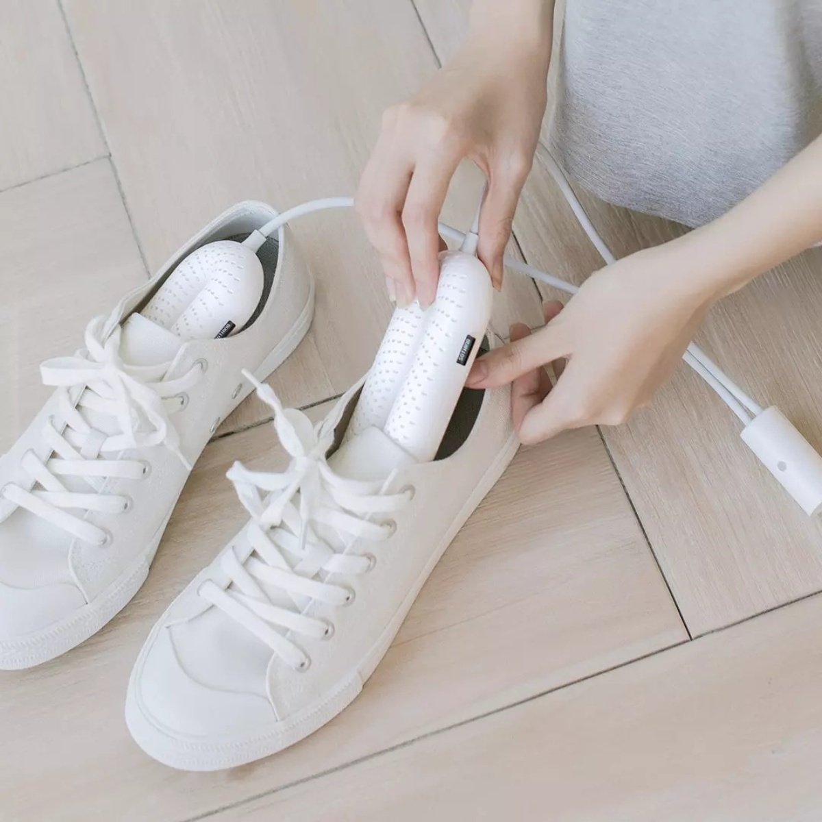 Eine Person steckt einen Schuhtrockner in einen weißen Sneaker. Ein weiterer weißer Sneaker liegt in der Nähe auf einem Holzboden.