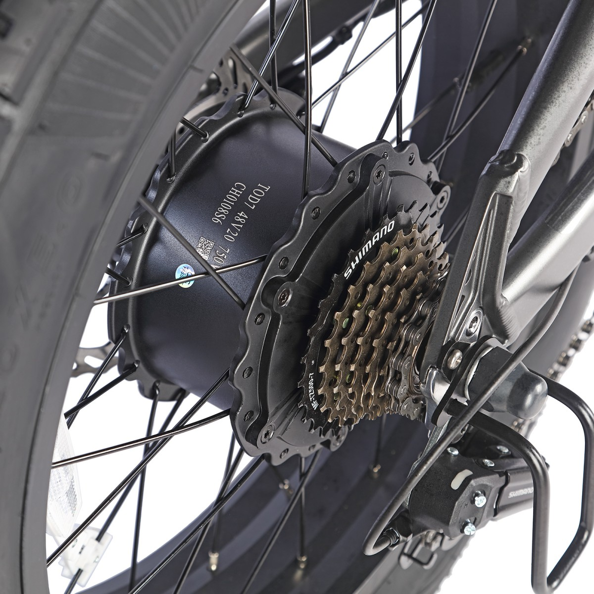 Zbliżenie koła roweru z systemem przerzutek Shimano. Czarne koło ma wiele szprych i jest na białym tle.