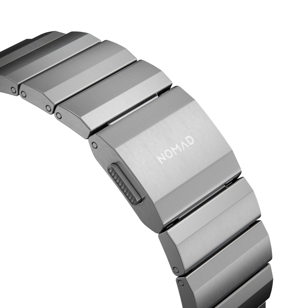 Primo piano di un cinturino d'orologio argentato con la scritta 'NOMAD' sulla chiusura. Il cinturino ha una finitura in metallo spazzolato ed è curvo.