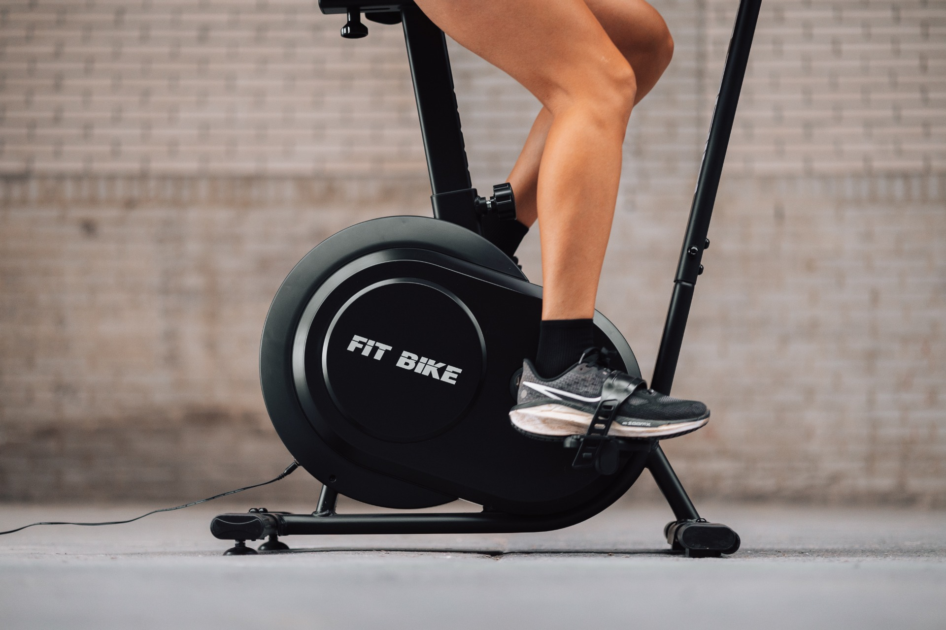 A person is shown exercising on a black stationary bike. The bike has 'FIT BIKE' on it. They wear a sneaker.