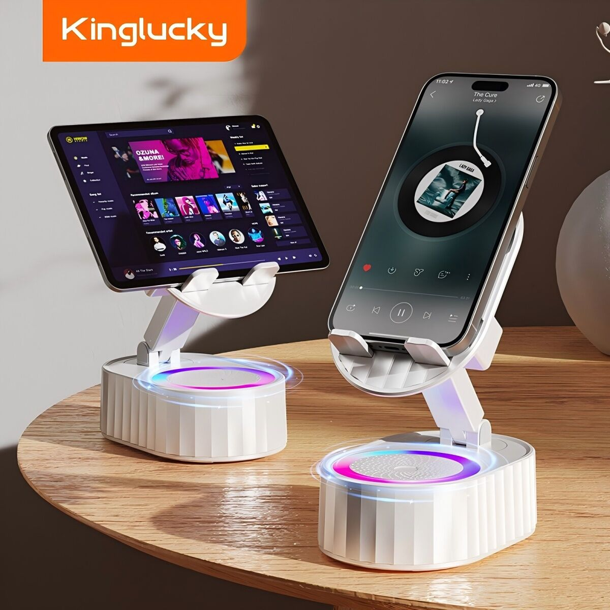 Due supporti telefonici bianchi con dispositivi su un tavolo di legno. Uno tiene un tablet, l'altro un telefono, entrambi mostrano contenuti.