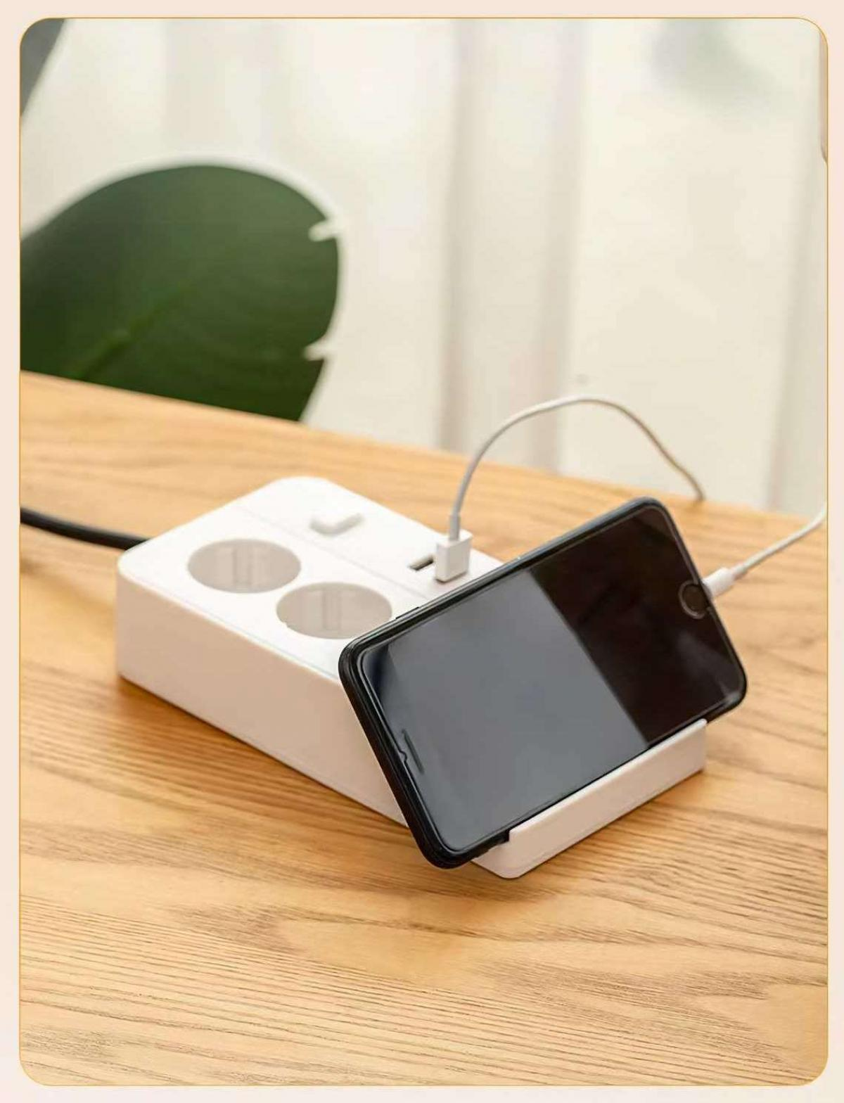 Ein schwarzes Smartphone, das an einem weißen Mehrfachstecker aufgeladen wird. Das Telefon befindet sich auf einer Holzoberfläche.