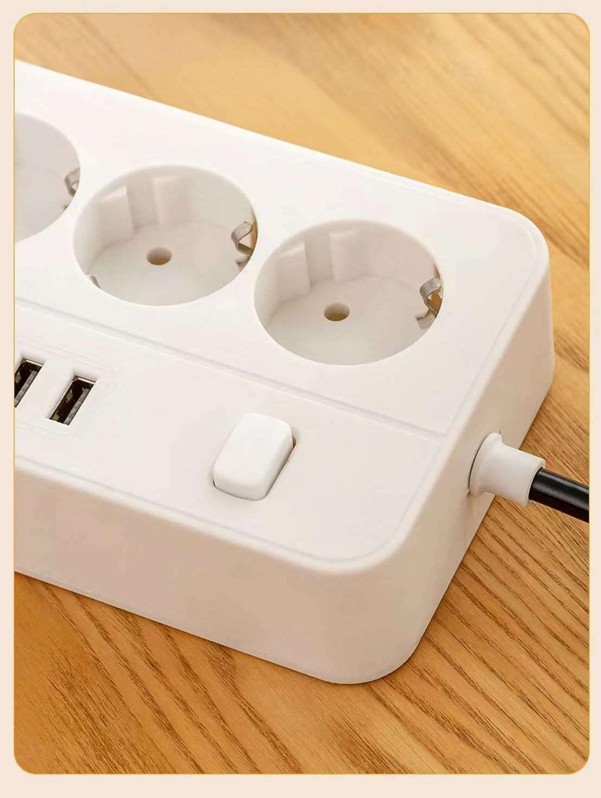 Eine weiße Steckdosenleiste mit drei Steckdosen, USB-Anschlüssen und einem Schalter. Sie liegt auf einer Holzoberfläche. Ein schwarzes Kabel geht davon aus.