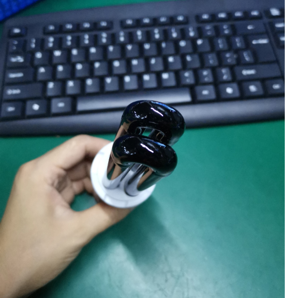 Eine Hand hält eine schwarze Glühbirne mit weißem Sockel. Im Hintergrund befindet sich eine Tastatur auf grüner Oberfläche.