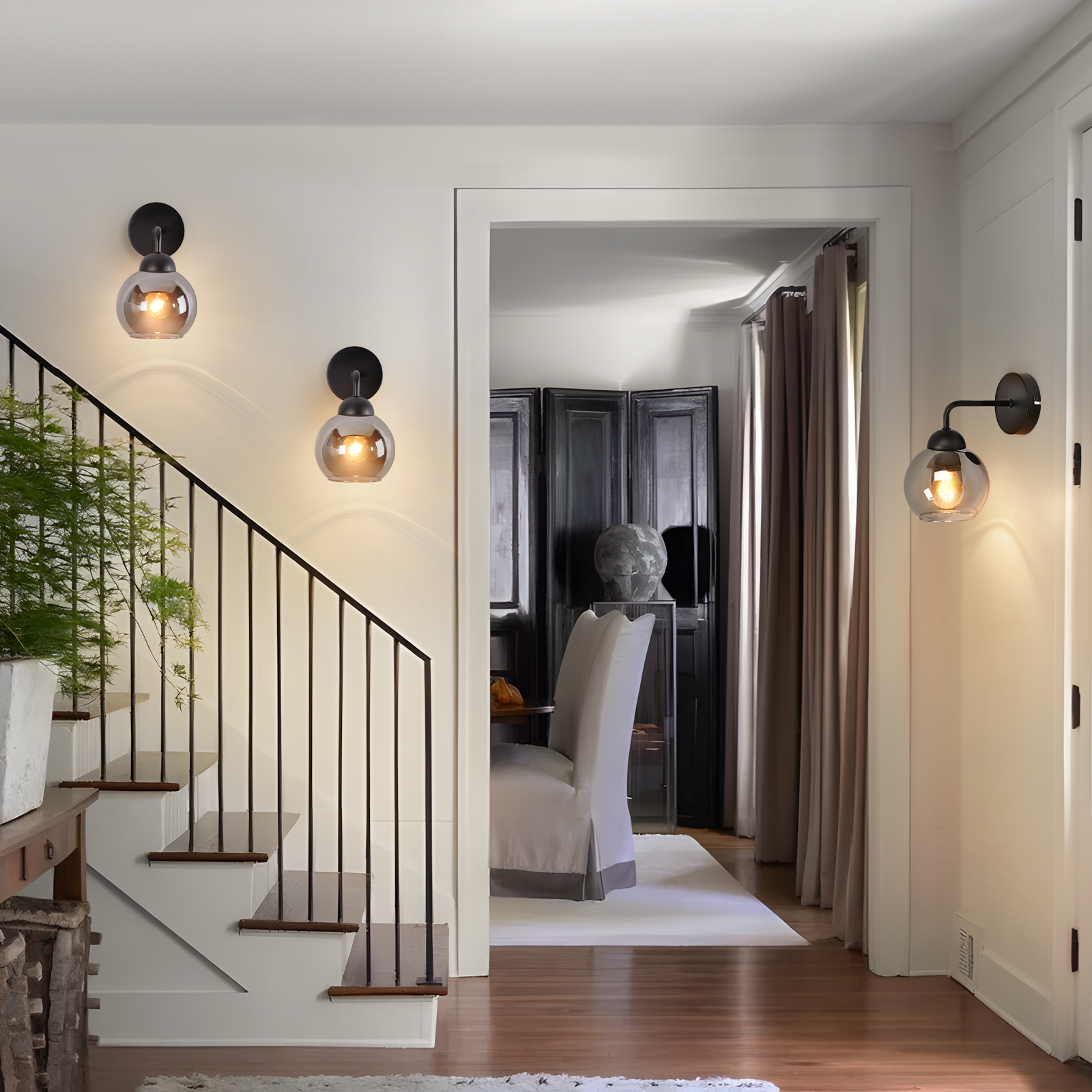 Un corridoio con scale e lampade da parete. Attraverso la porta, una sala da pranzo con tavolo e sedie.