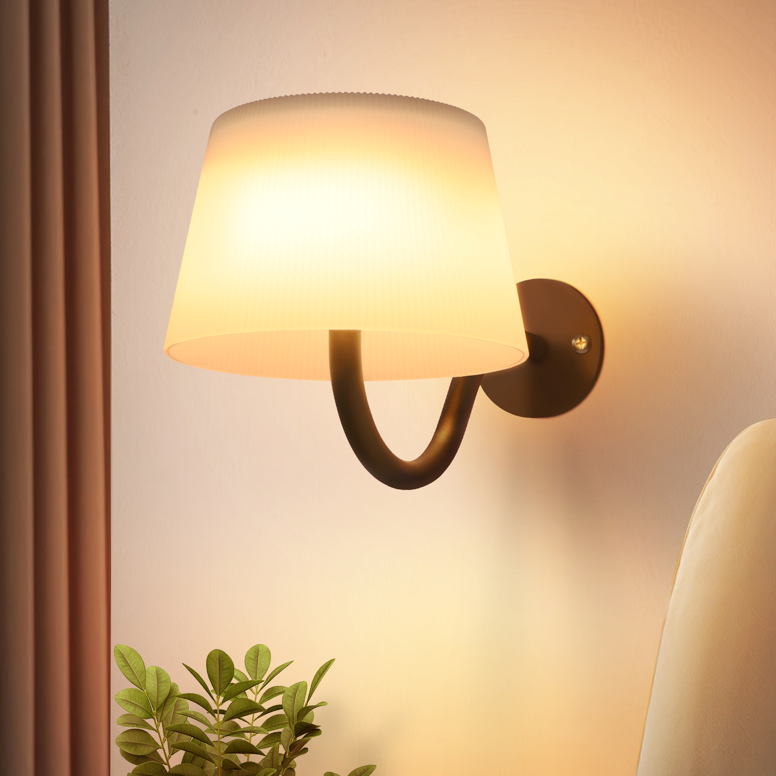 Una lampada da parete con paralume. Una pianta in primo piano. Il muro è chiaro.