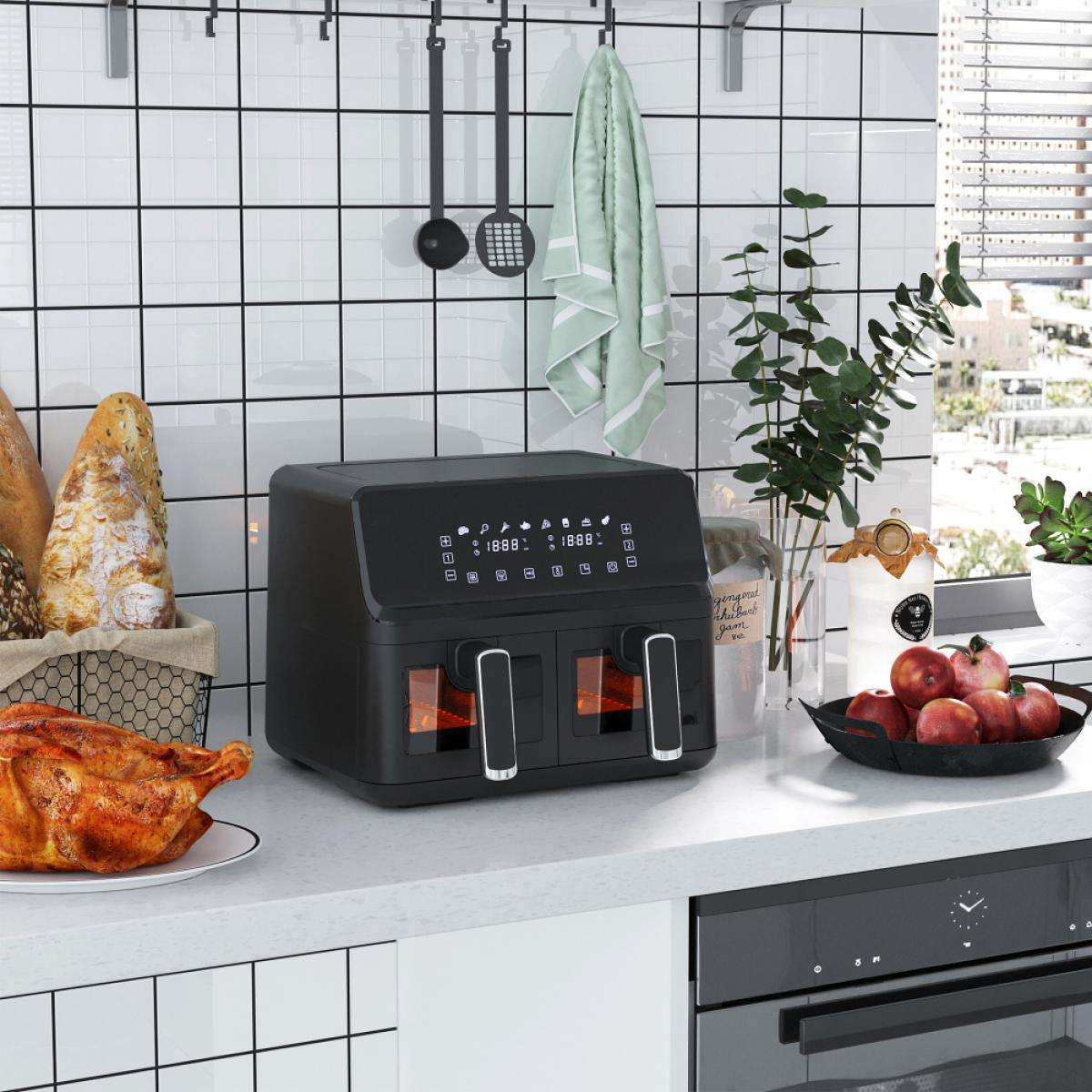 Eine Küchenszene mit einem schwarzen Airfryer, einem Brathähnchen, einem Brotkorb und einer Schale mit Äpfeln. Grünes Handtuch hängt.