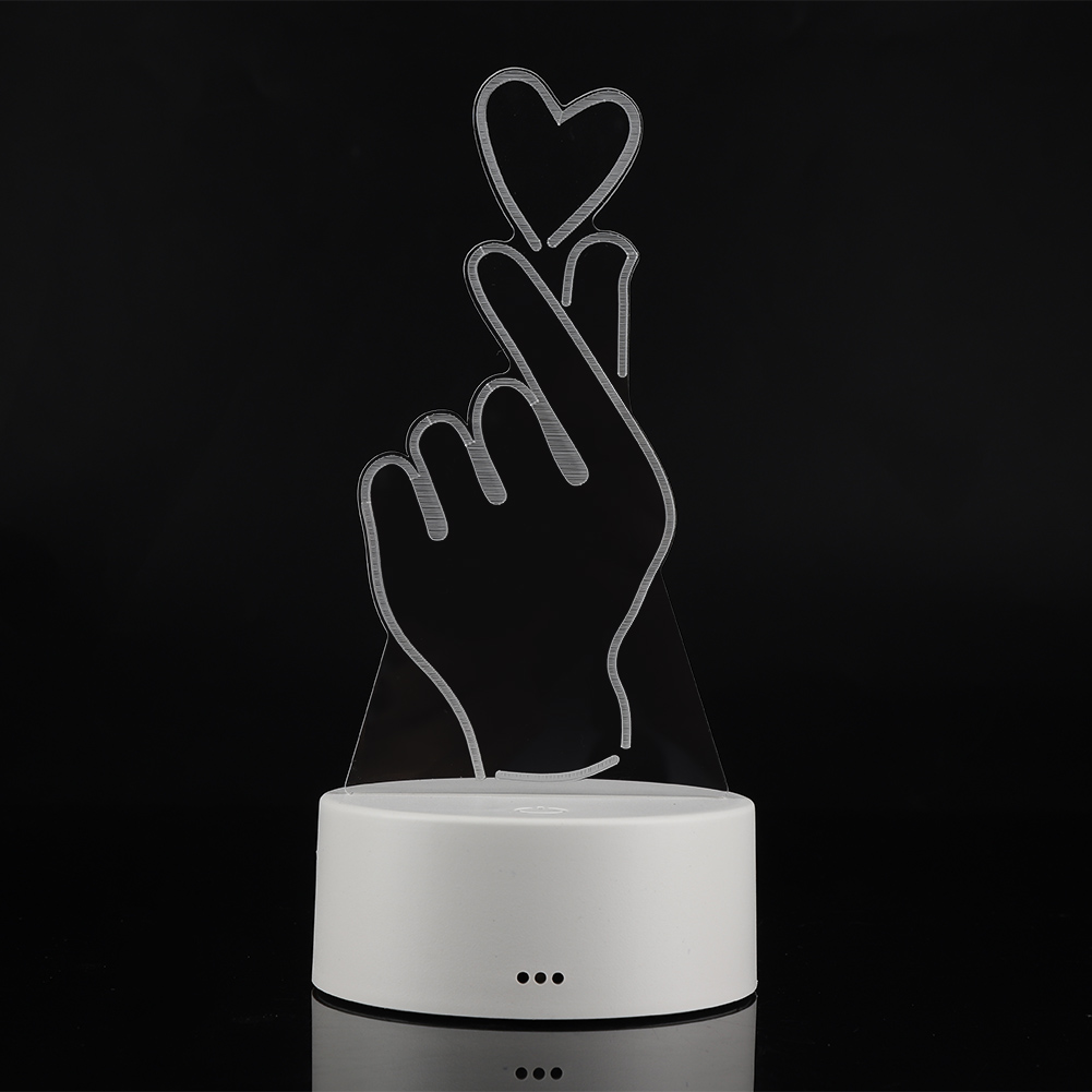 Eine herzförmige Handgestenlampe. Transparente Handkontur mit Herz und weißem Sockel auf schwarzem Hintergrund.