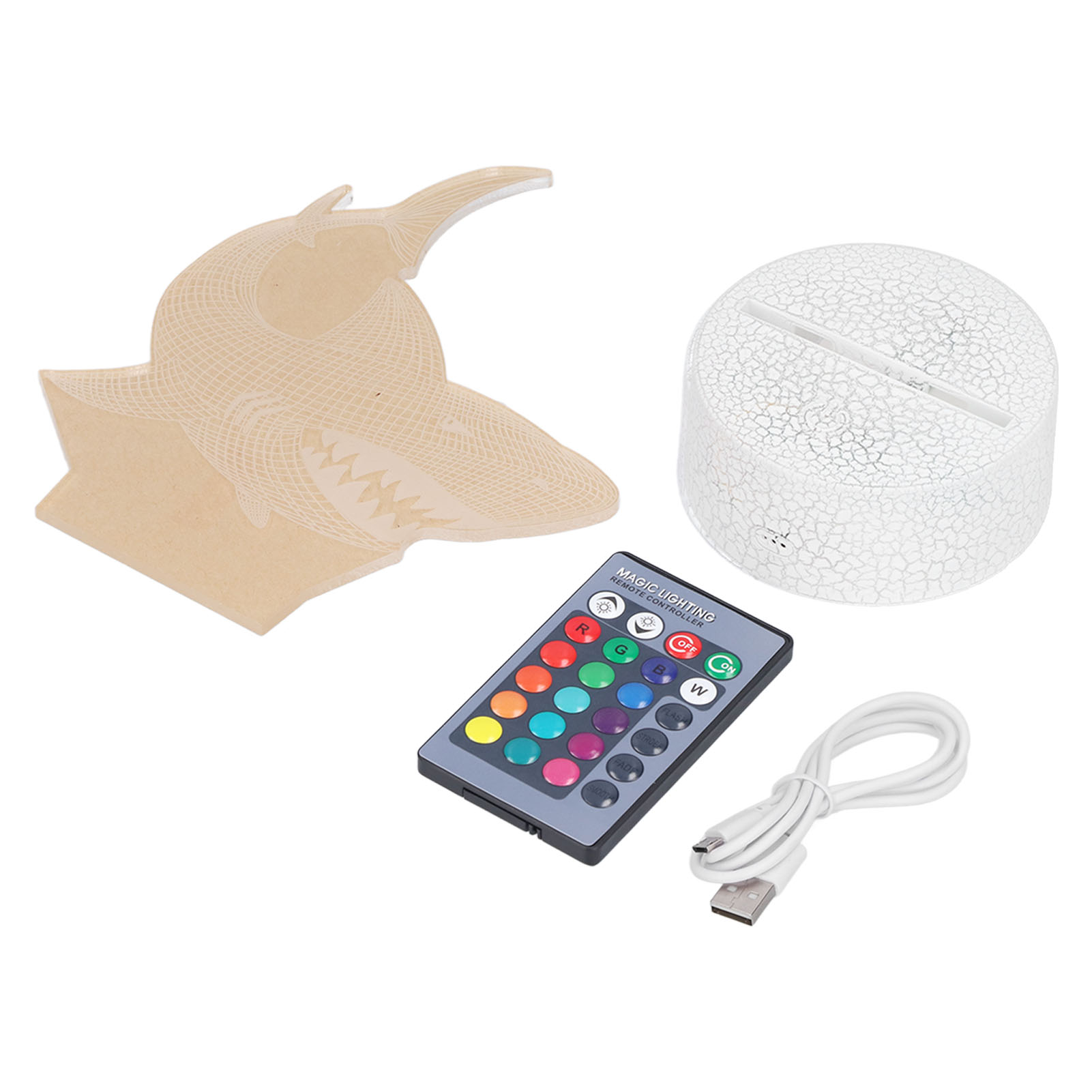Eine haiförmige Lampe, eine Basis, eine Fernbedienung und ein USB-Kabel liegen auf einer weißen Oberfläche. Der Hai ist beige.