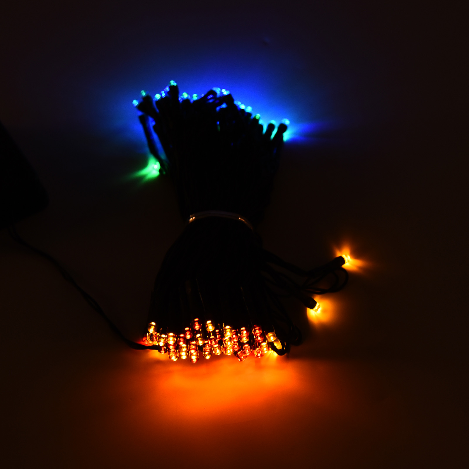Nahaufnahme von Lichterketten mit blauen, grünen und orangen Lichtern. Dunkle Szene, nur die Lichter leuchten.