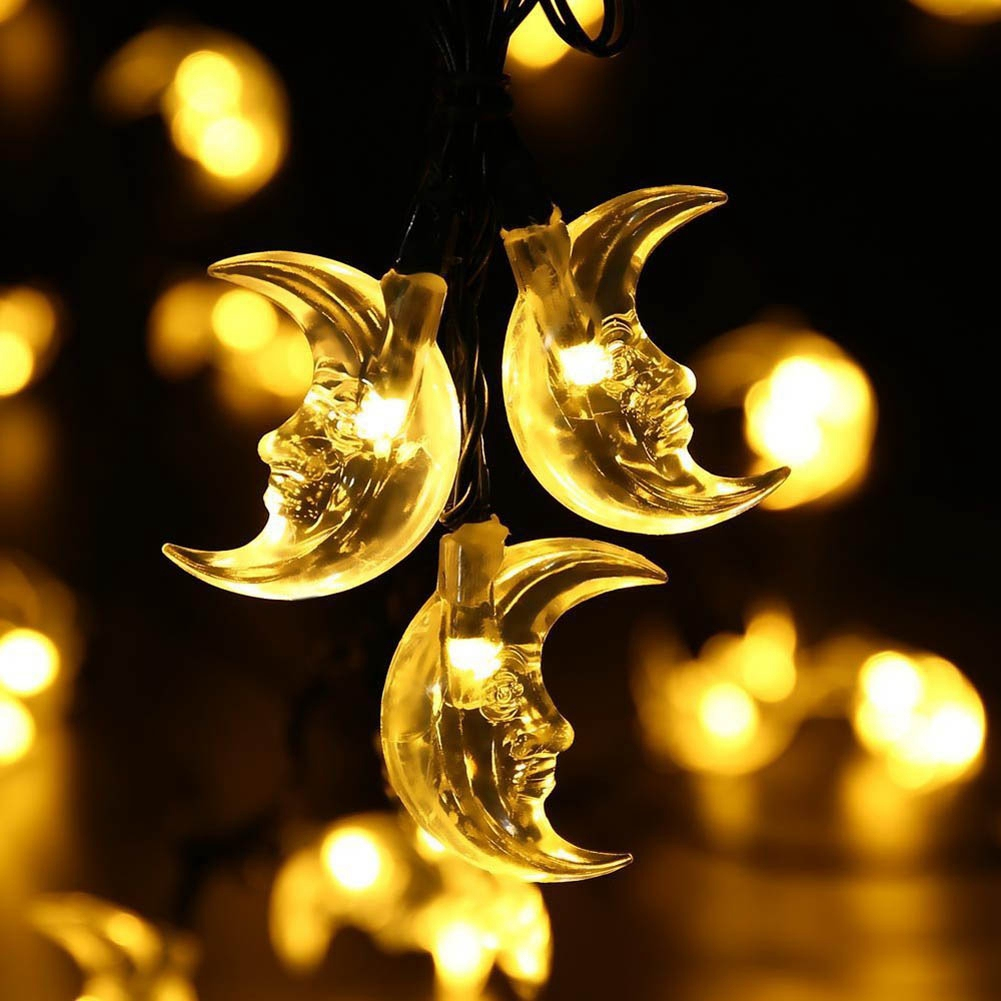 Nahaufnahme von leuchtenden Halbmond-Lichterketten mit Gesichtern. Hintergrund zeigt Bokeh-Lichter auf dunkler Oberfläche.