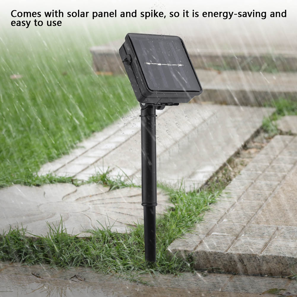 Schwarzes Solarpanel auf einem schwarzen Pfahl in einem Garten. Es regnet. Gehweg und Gras sind im Hintergrund.