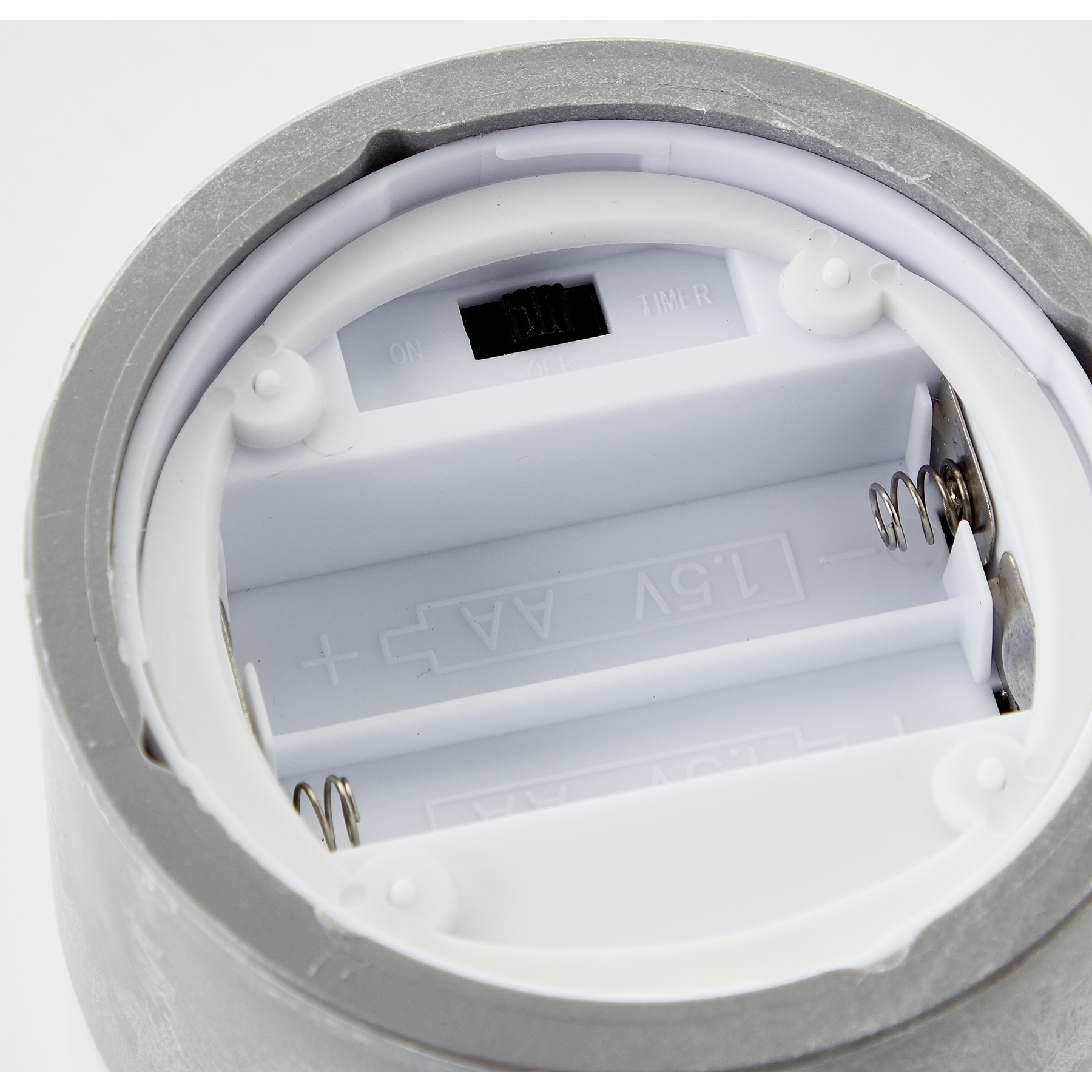 Nahaufnahme eines Batteriefachs. Graues Gehäuse umgibt einen weißen Innenraum mit Platz für AA-Batterien und einen Ein-/Aus-Timerschalter.