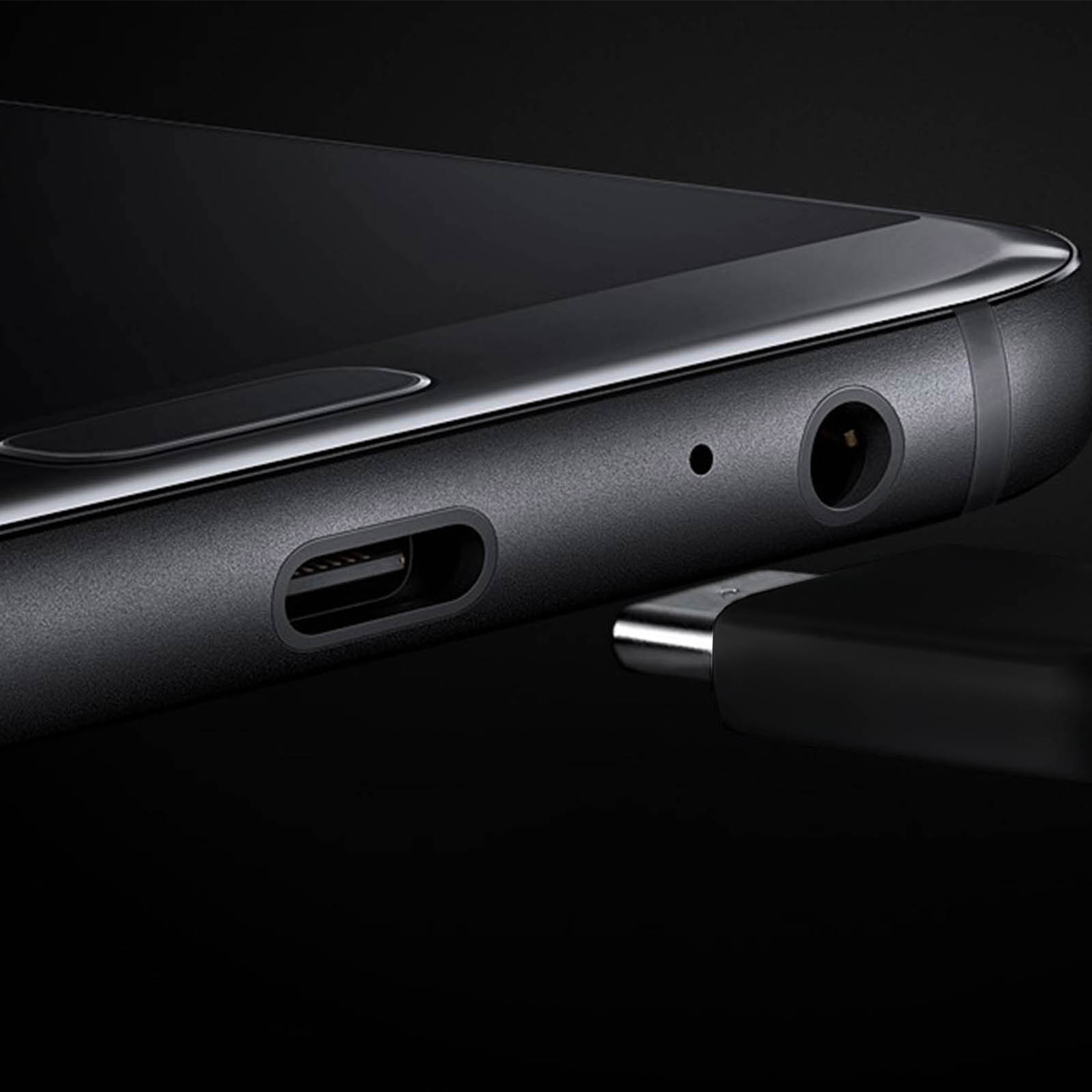 Primo piano del bordo inferiore di uno smartphone nero. Porte USB-C, jack per cuffie e cavo di ricarica visibili.