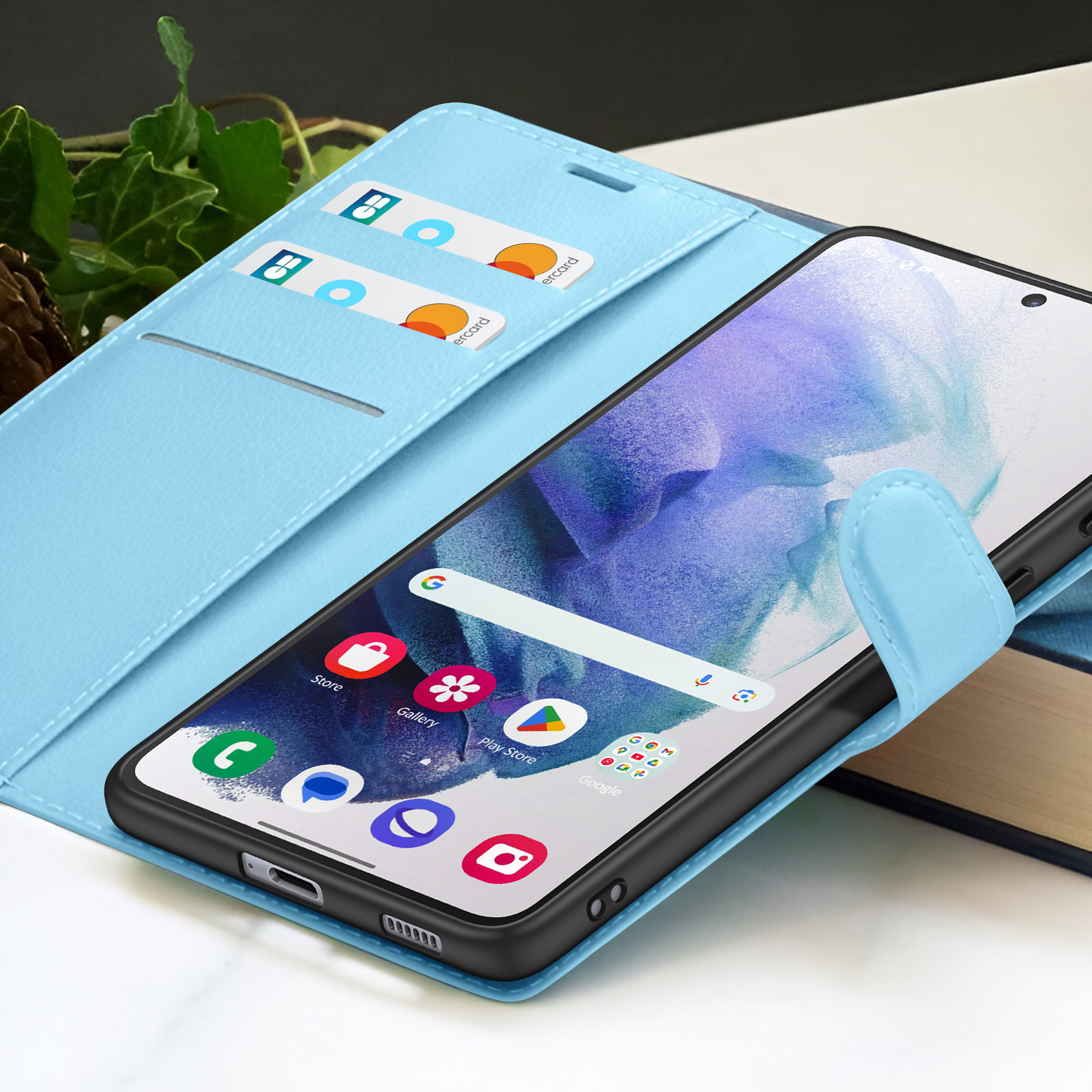 Un smartphone dans un étui portefeuille bleu clair avec des fentes pour cartes de crédit, des applications visibles et un livre en arrière-plan.