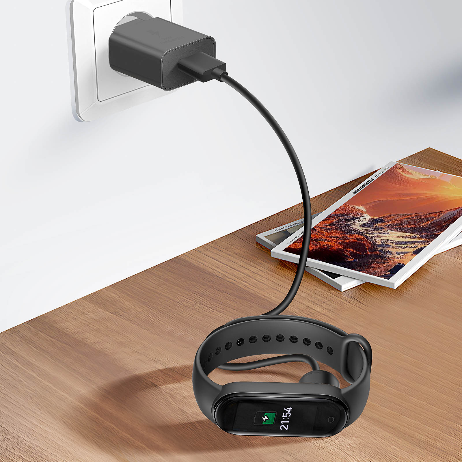 Fitness tracker nero in carica su tavolo in legno. Caricatore collegato alla parete. Riviste sullo sfondo.
