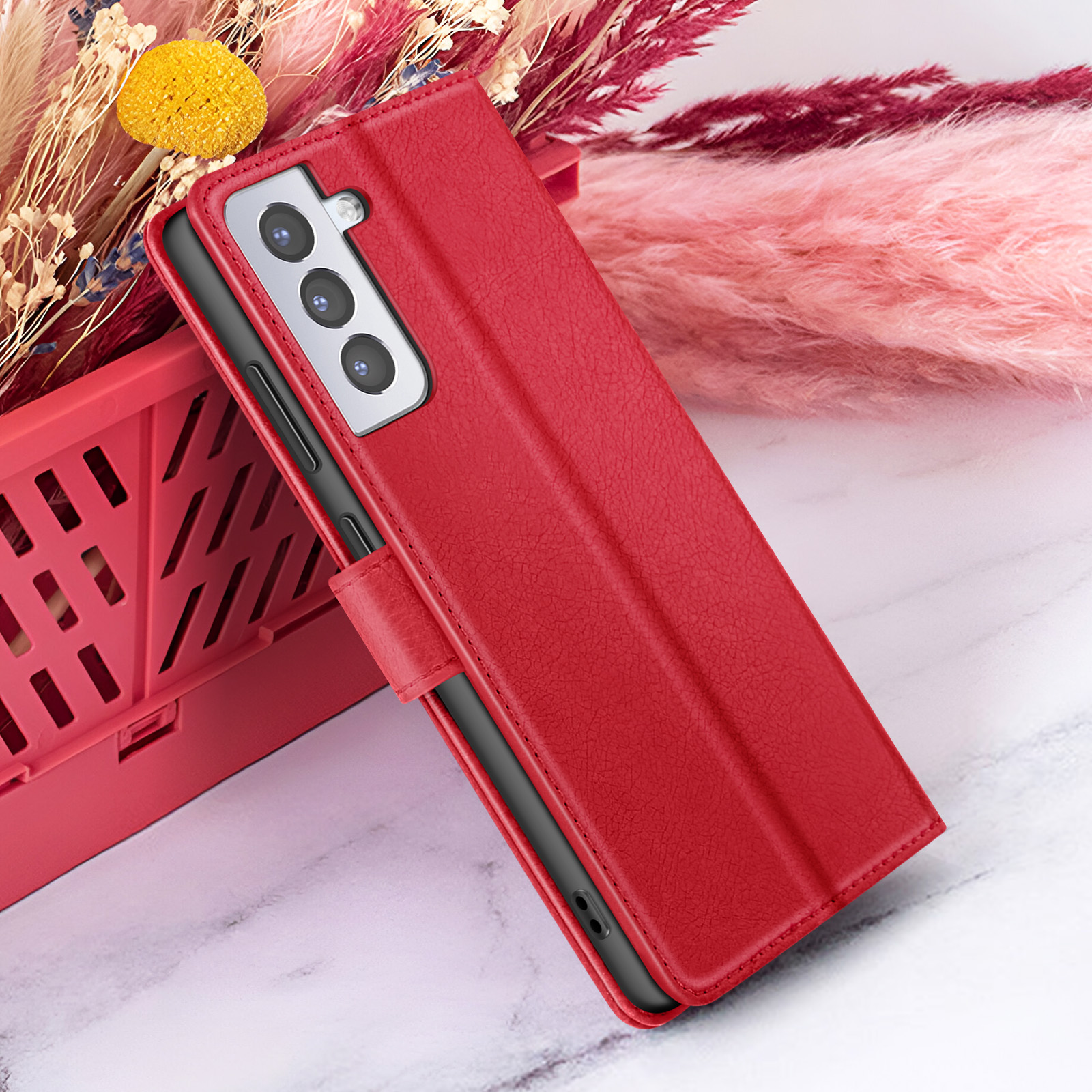 Un étui de téléphone rouge avec un téléphone à l'intérieur, placé sur une surface en marbre, à côté d'un panier rouge et des fleurs.