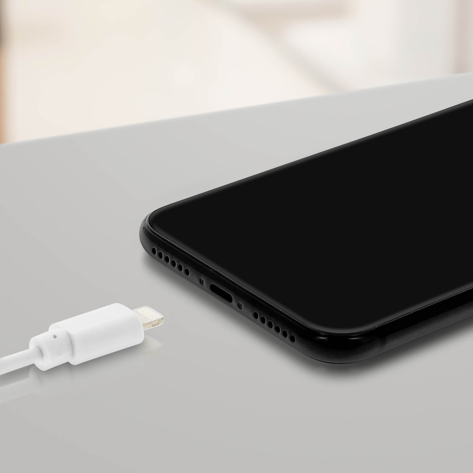 Un smartphone noir avec un câble de chargement blanc sur une surface gris clair. Le téléphone est partiellement visible.